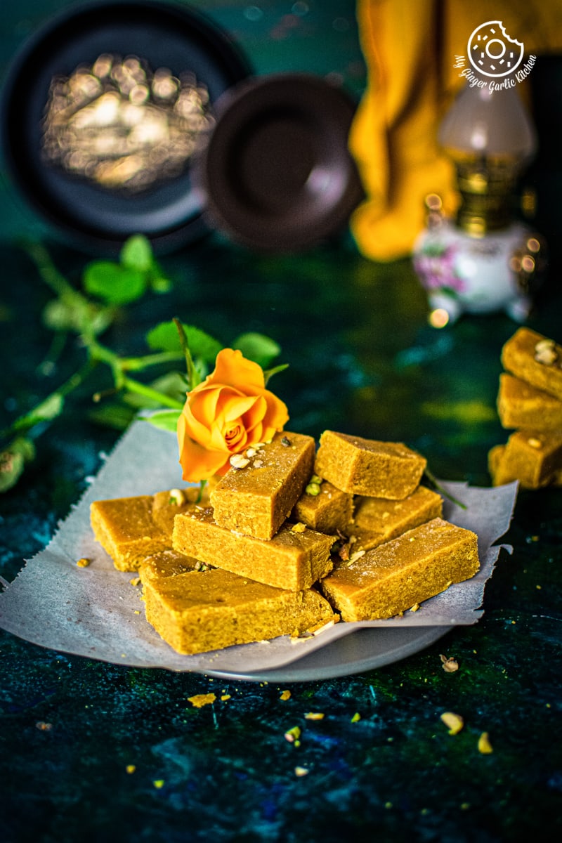 ghee mysore pak in served in a ceramic plate with a deep yellow rose on the side