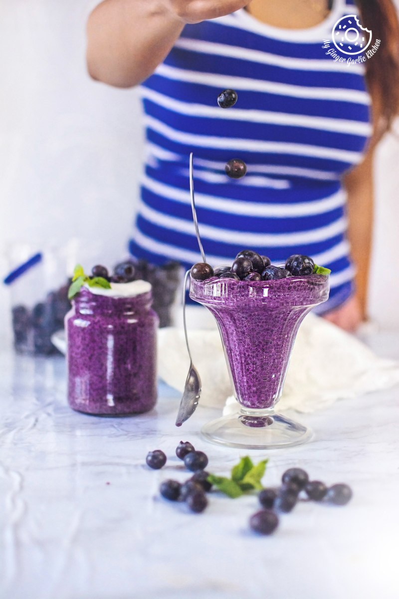 a gril dropping blueberries on a blueberry chia seed pudding glass