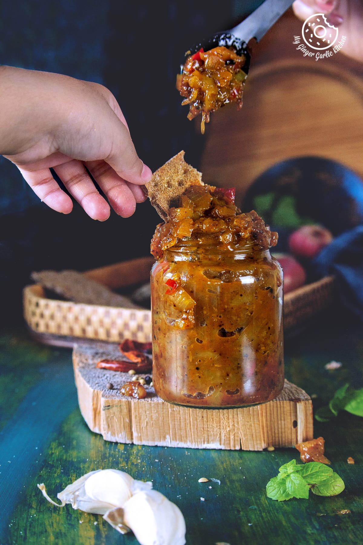 a hand on the peach chutney in a glass jar and a spoon in background