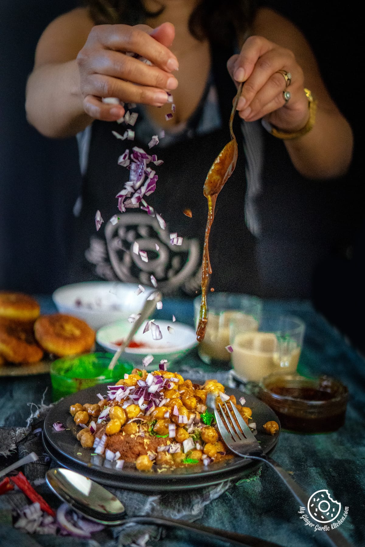 a female sprinkling onions and pouring tamarind chutney chana masala over chole aloo tikki chaat