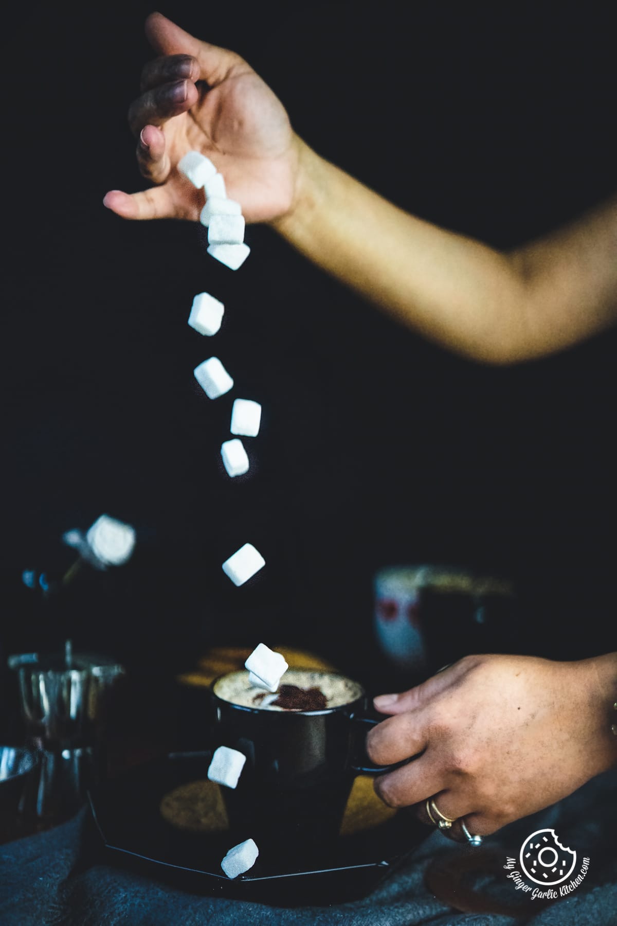 a hand pouring sugar cubes over indian cappuccino coffee