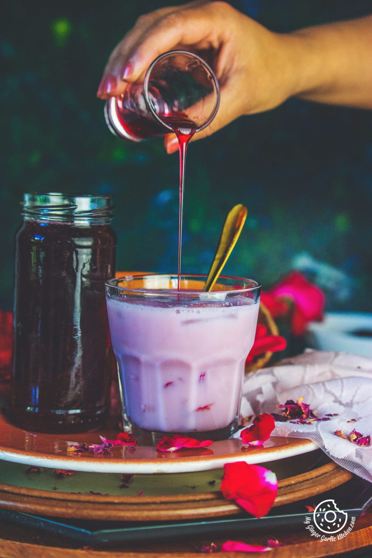 a female pouring rose syrup over rose milk glass