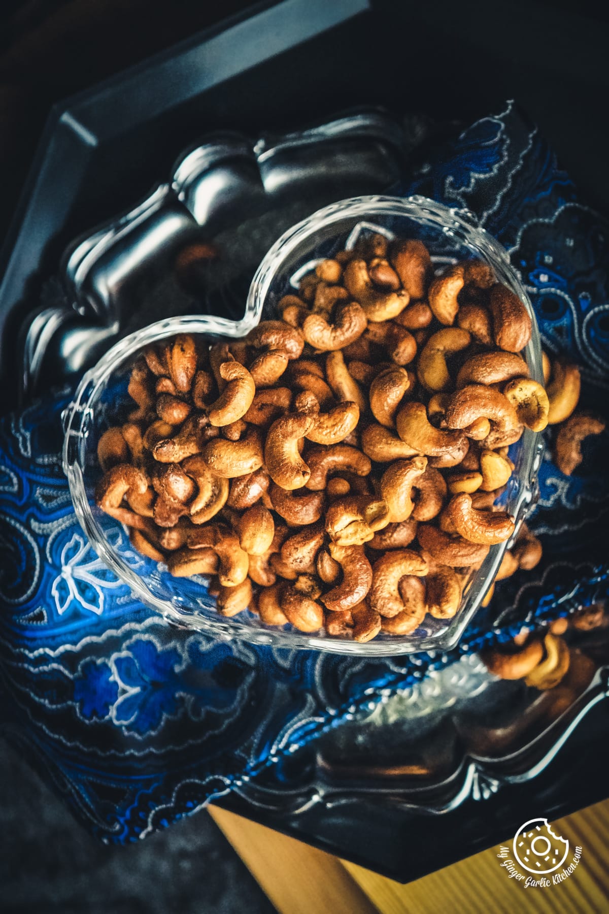 overhead shot of masala kaju (spicy roasted cashew nuts) served in a heart shape transparent bowl