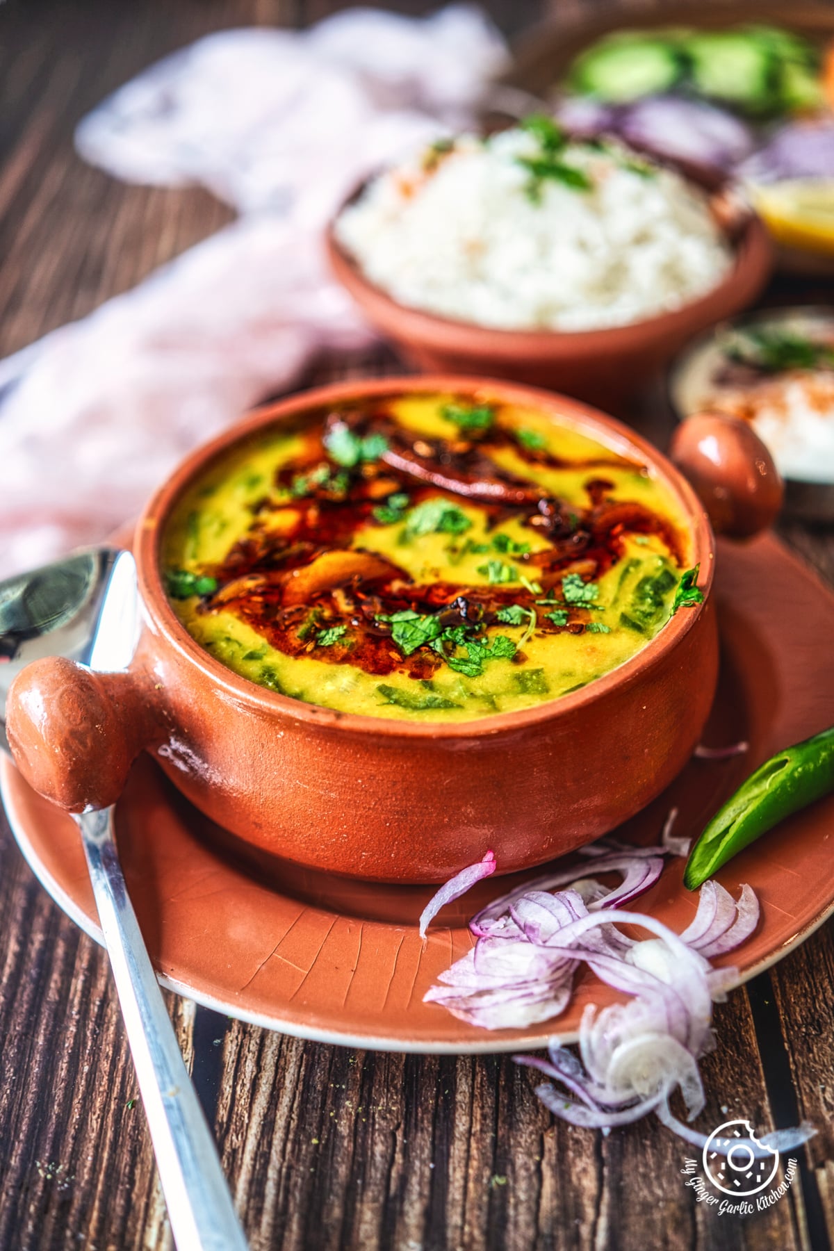 dal palak served in a terra cotta bowl with sliced onions and green chili on the side