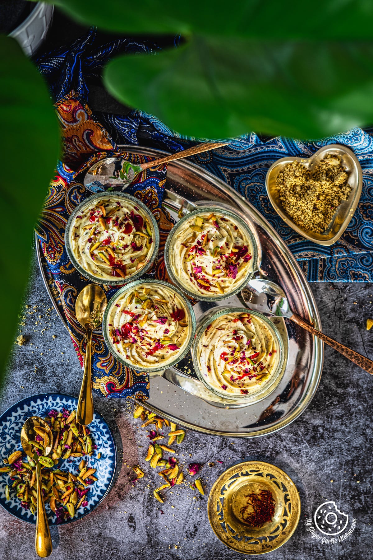 overhead shot of thandai shrikand bowls in a metal tray and saffron and pistachio plates are on the side