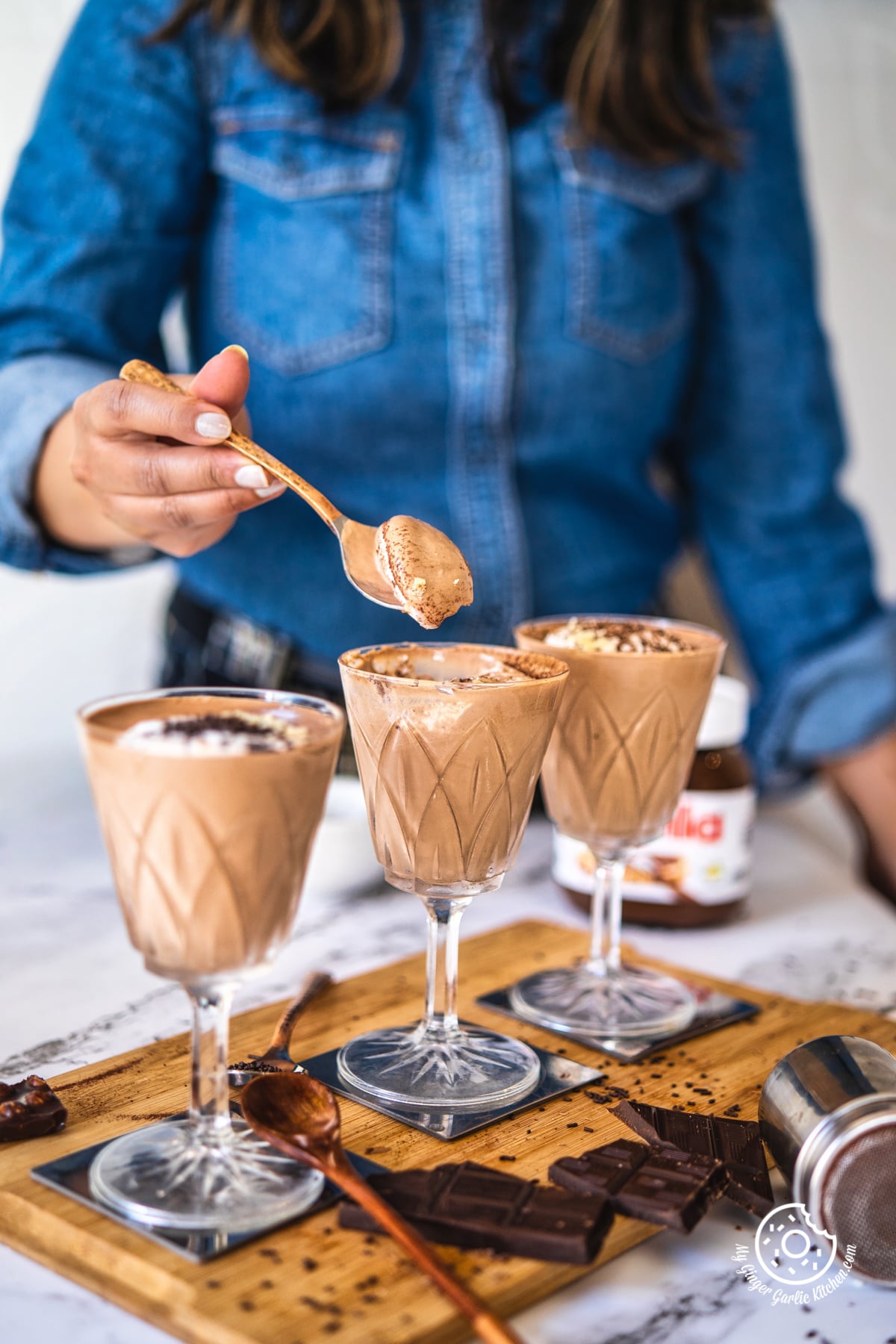 a female holding a spoon with nutella mousse over a nutella glass and 2 more glasses