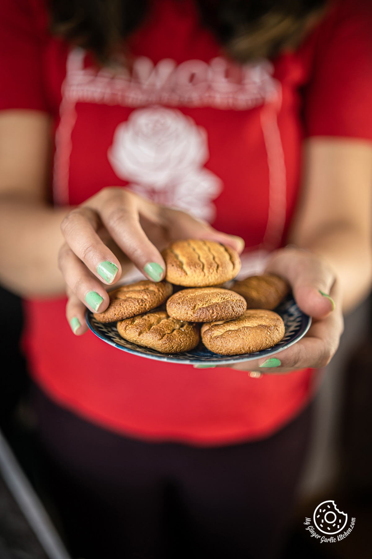 a female holding almond flour cookies plate with one hand and a cookie with other hand
