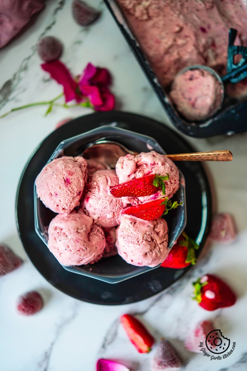 overhead shot of strawberry ice cream in a grey bowl and some strawberries on side