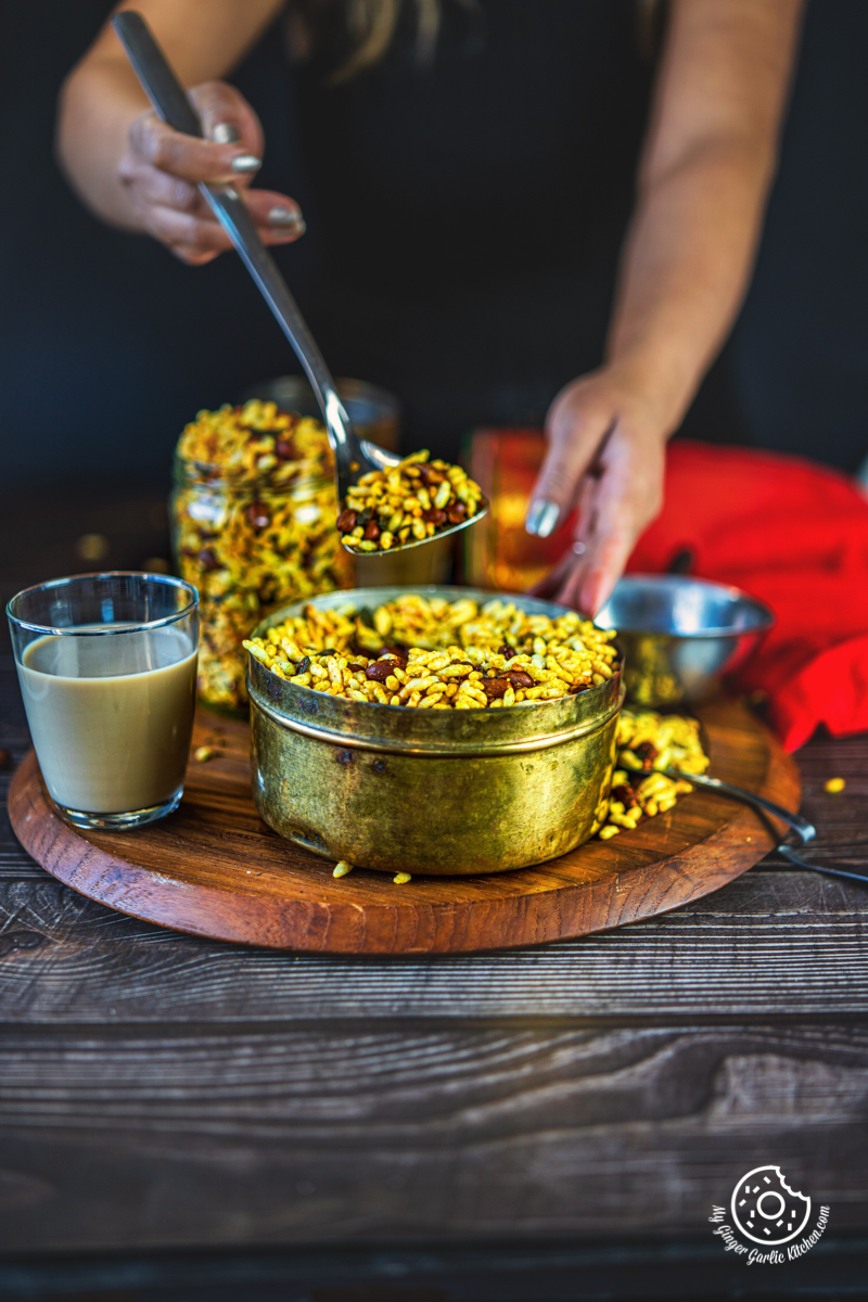 a female holding a spoon over an antique brass pot filled with murmura chivda | spicy puffed rice | murmura namkeen