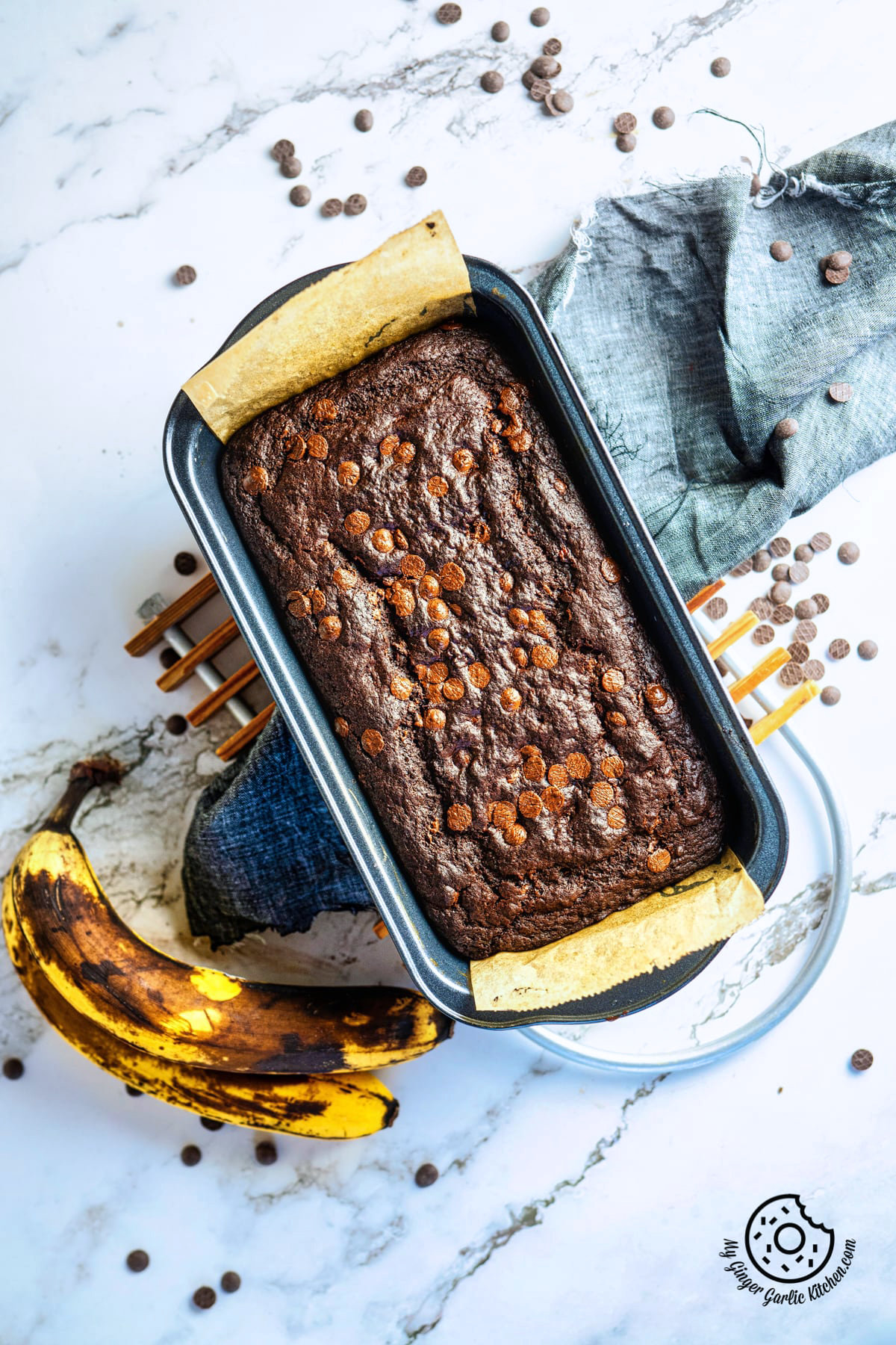 chocolate banana bread in a loaf pan and two ripe bananas on the side