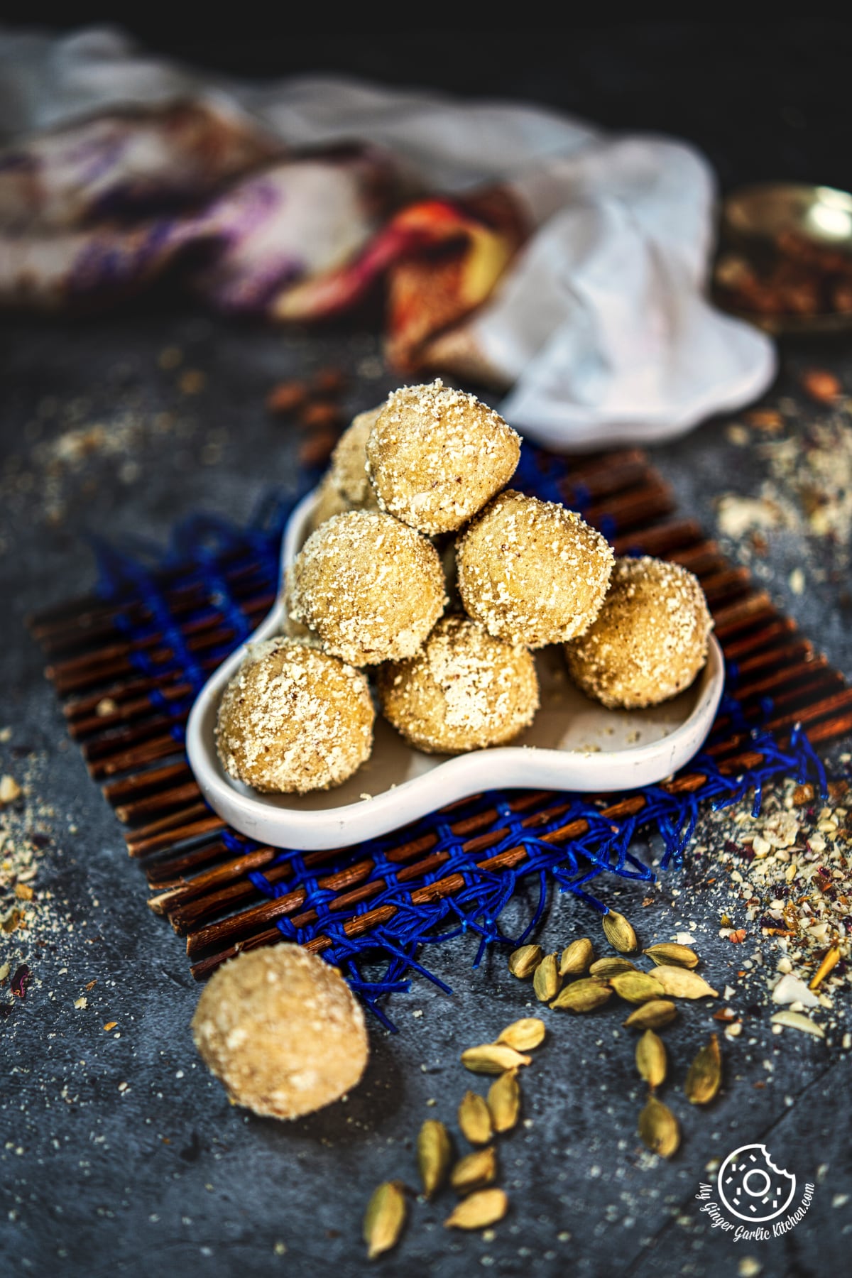 peanut ladoo in a white plate with green cardamom pods on the side