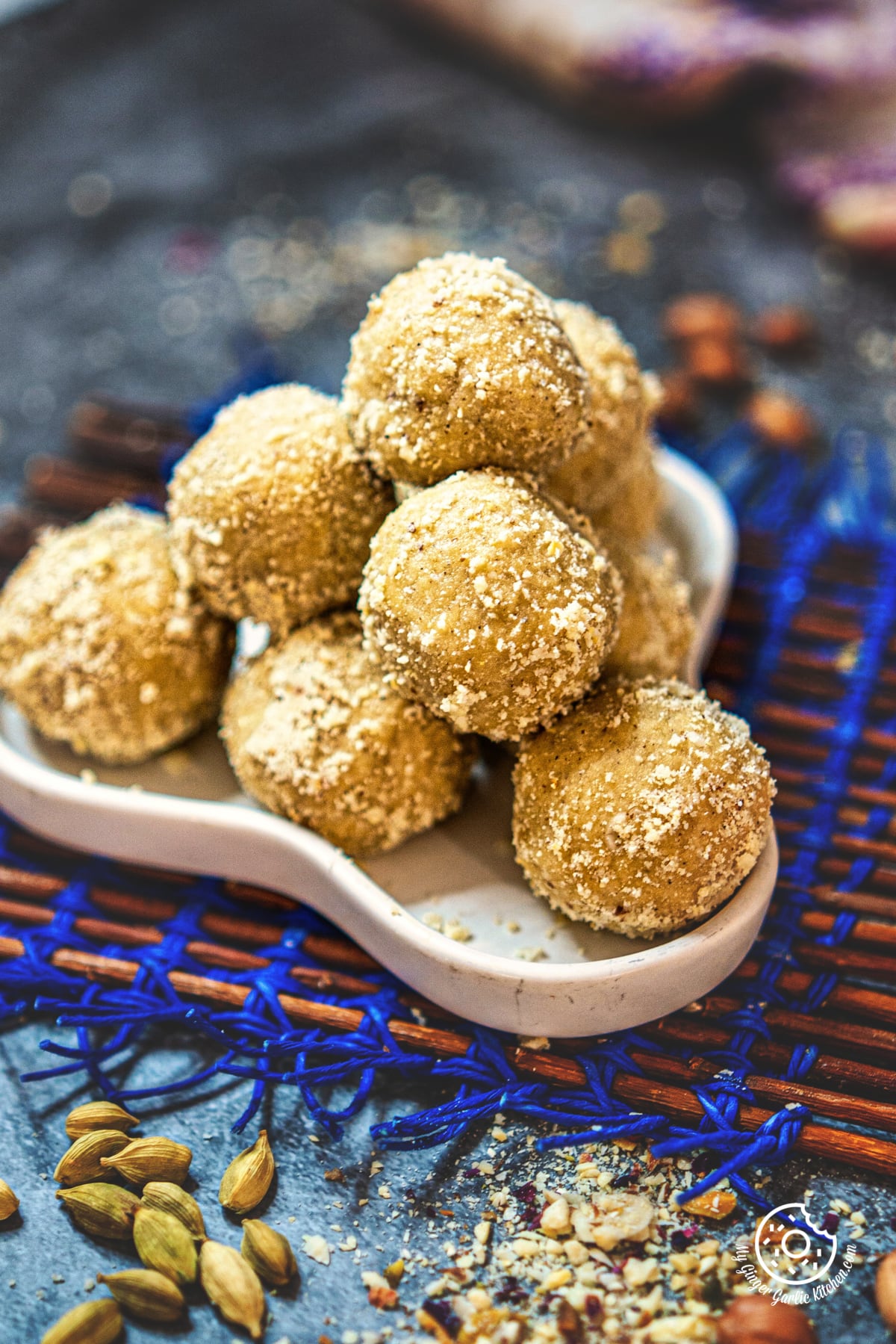 close up shot of peanut ladoos piled on a white plate with scattered green cardamom pods