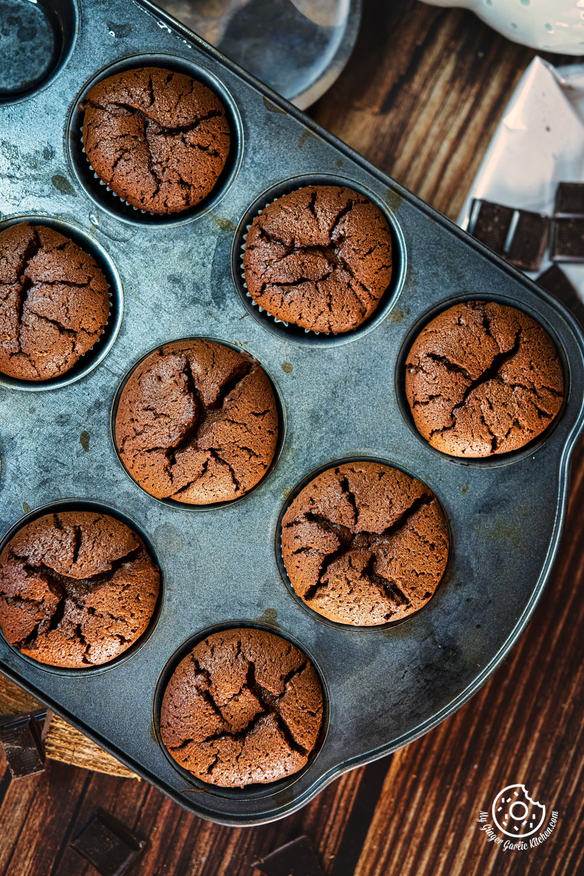 overhead shot of eight 2 ingredient chocolate muffins on a natural wooden log and a person holding a muffin in the background