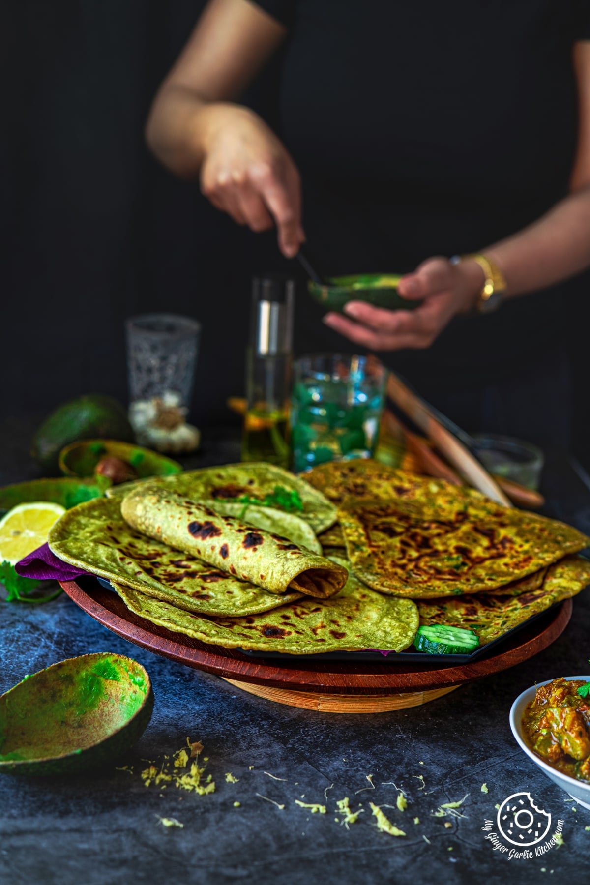 avocado parathas and avocado rotis in a wooden plate and a female scooping avocado pulp in the background