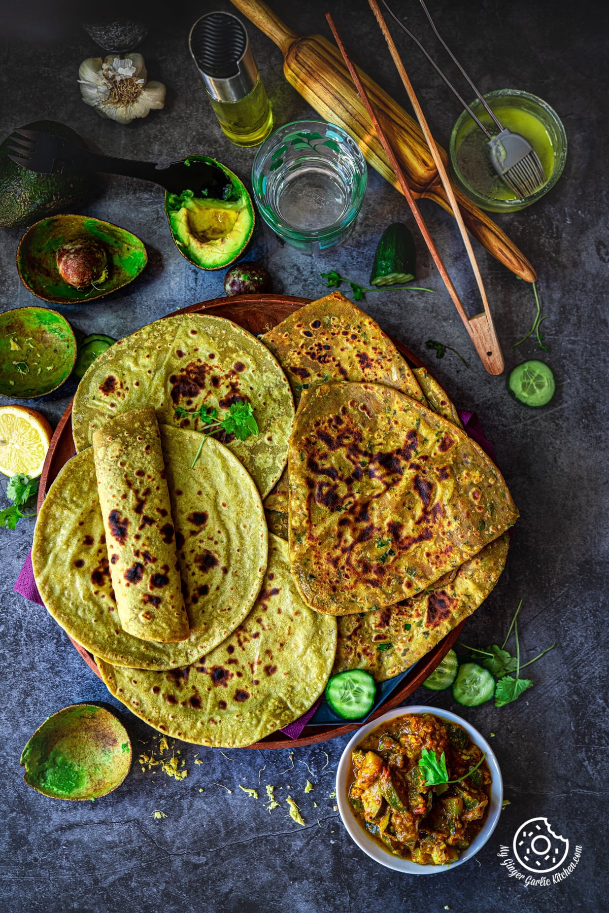 overhead shot of avocado paratha and avocado roti in a wooden plate with a curry bowl and avocado skin on the side