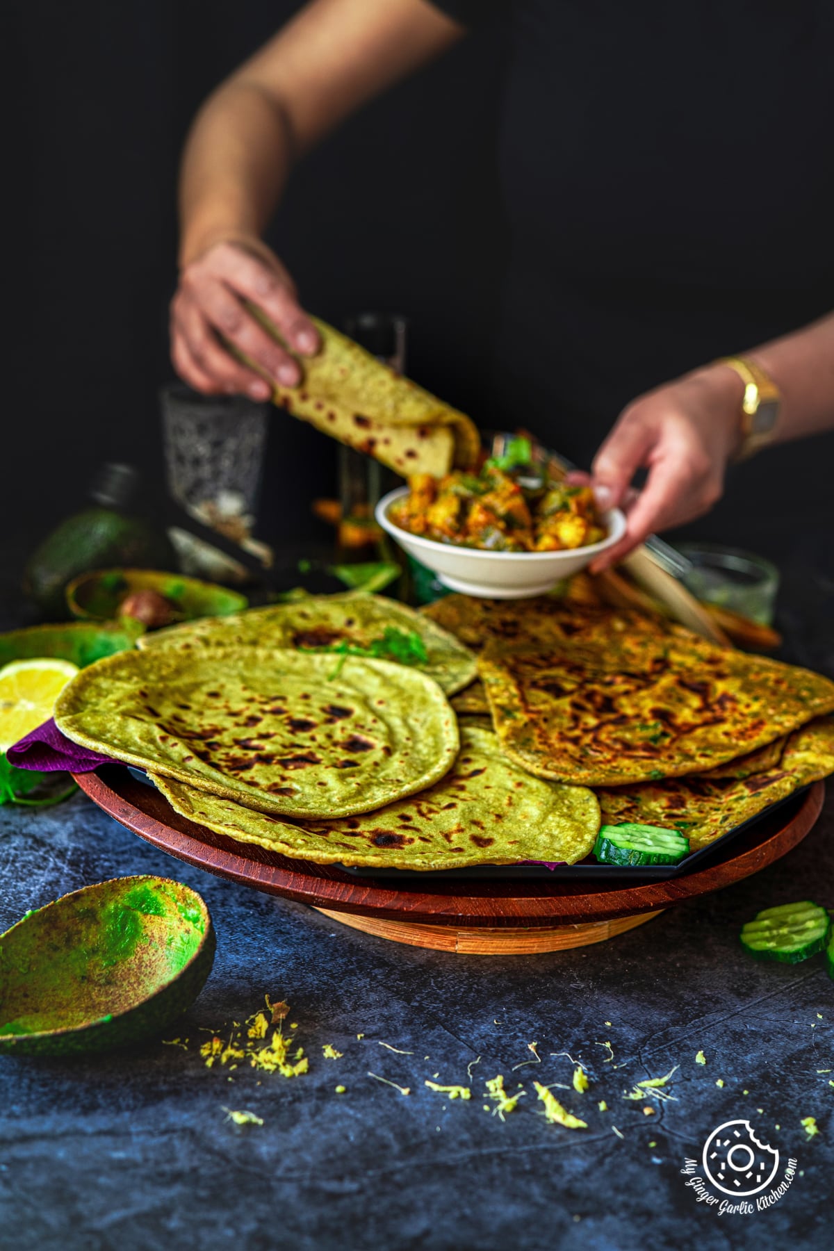 avocado parathas and avocado rotis in a wooden plate and a female holding a curry bowl and a rolled avocado roti with the other hand