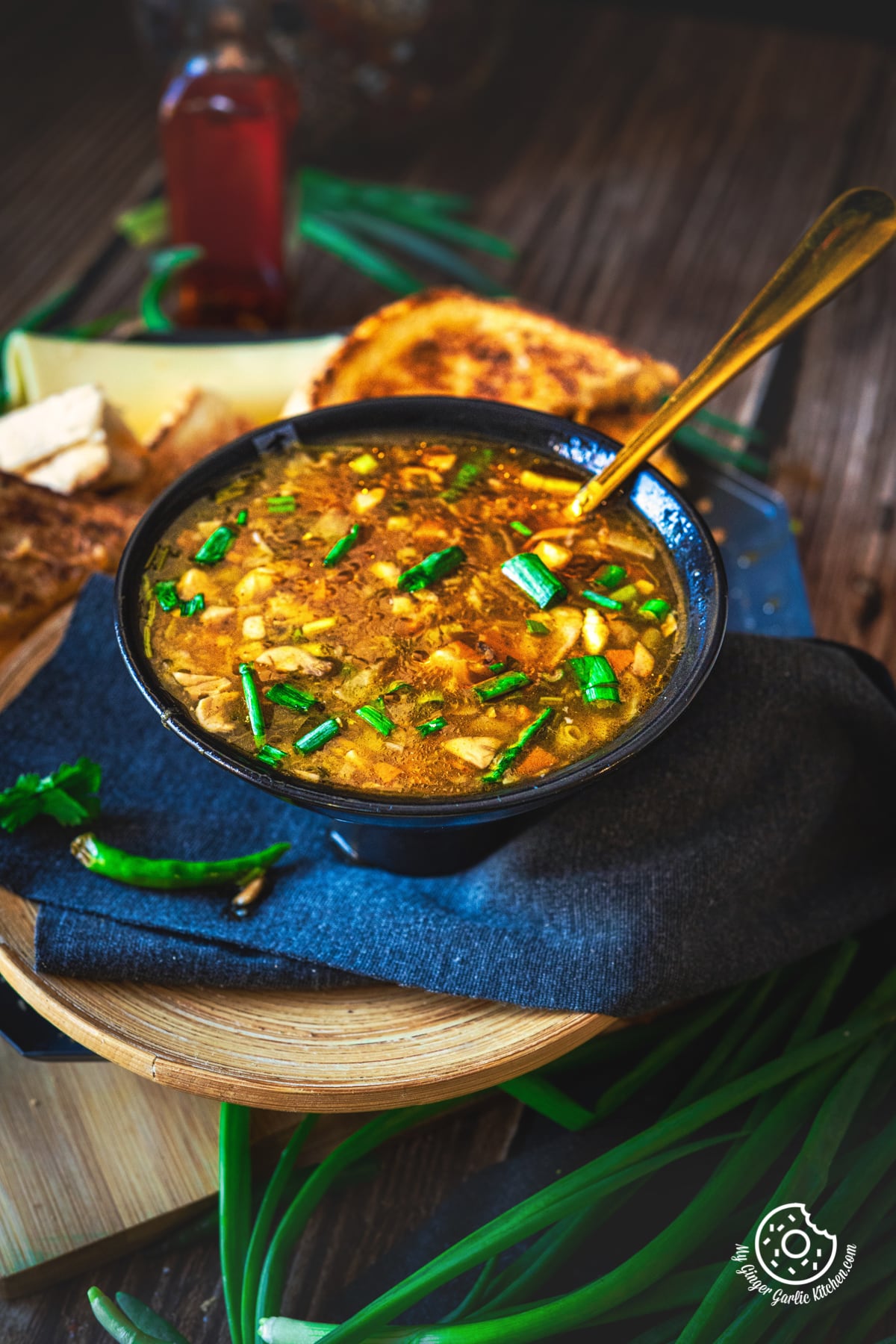 hot and sour soup garnished with spring onions in black ceramic bowl