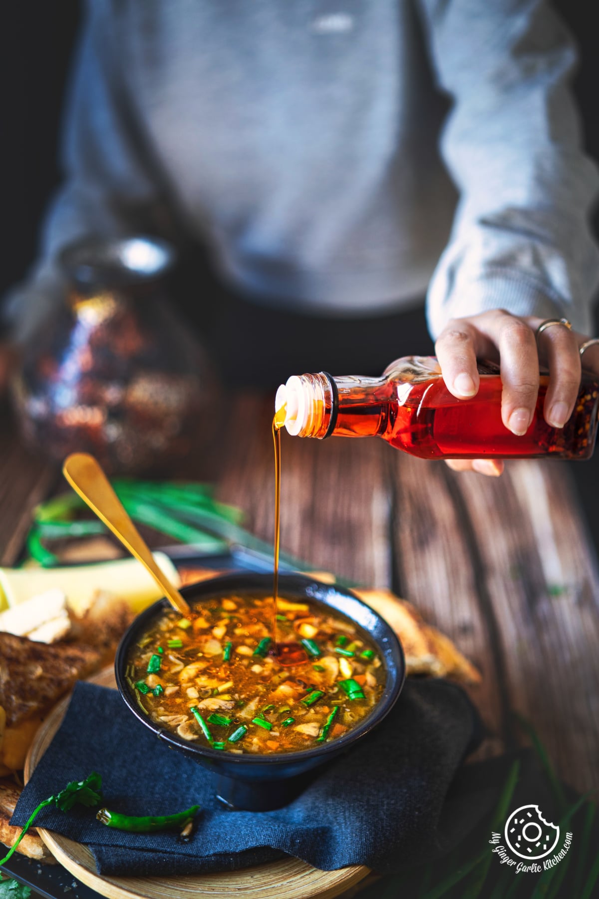 a female drizzling chili oil on a hot and sour soup bowl