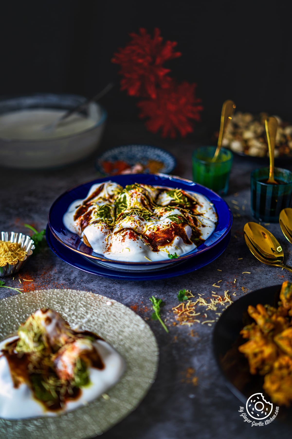 dahi vada topped with chutneys and sev in a blue glass plate with some sev and dahi vada on the side