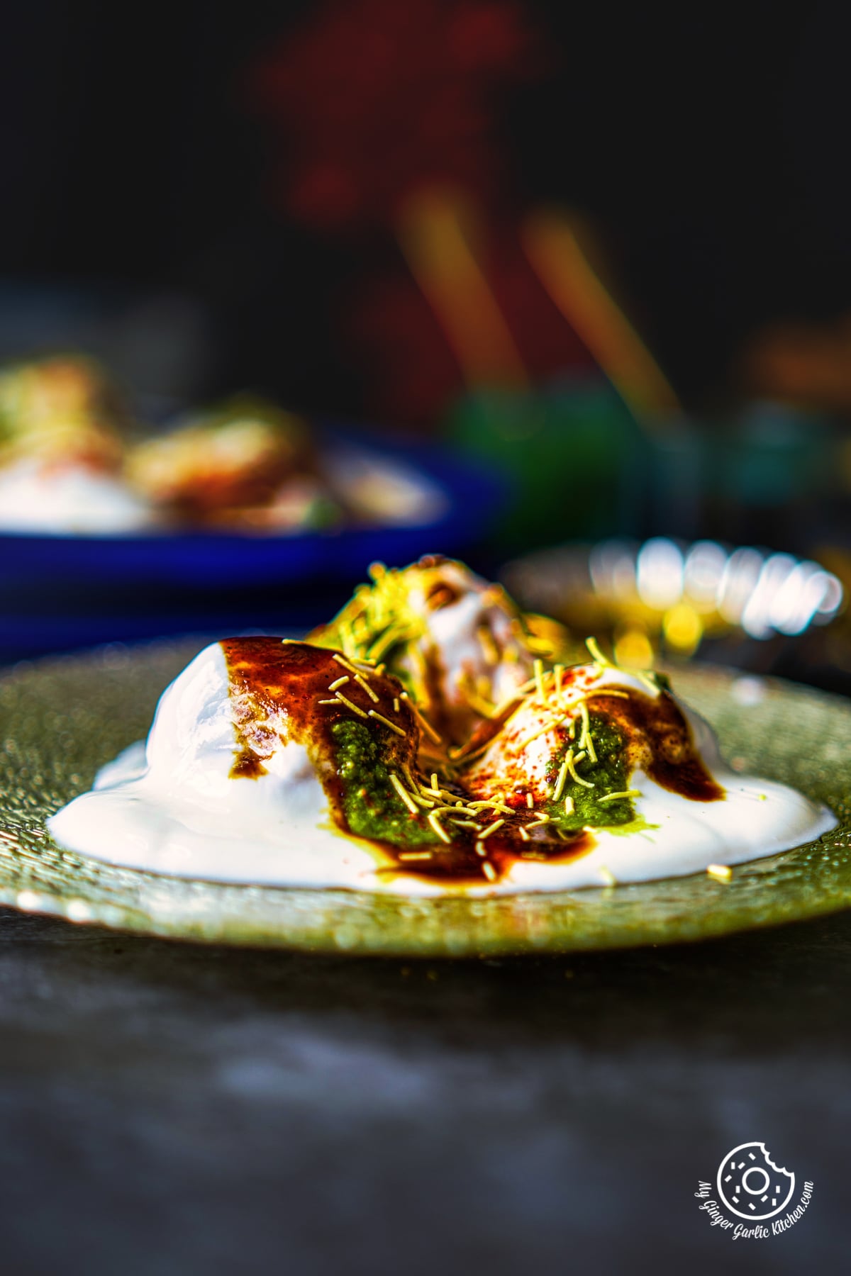 a closeup shot of three dahi vadas topped with chutneys and sev in a silver glass plate