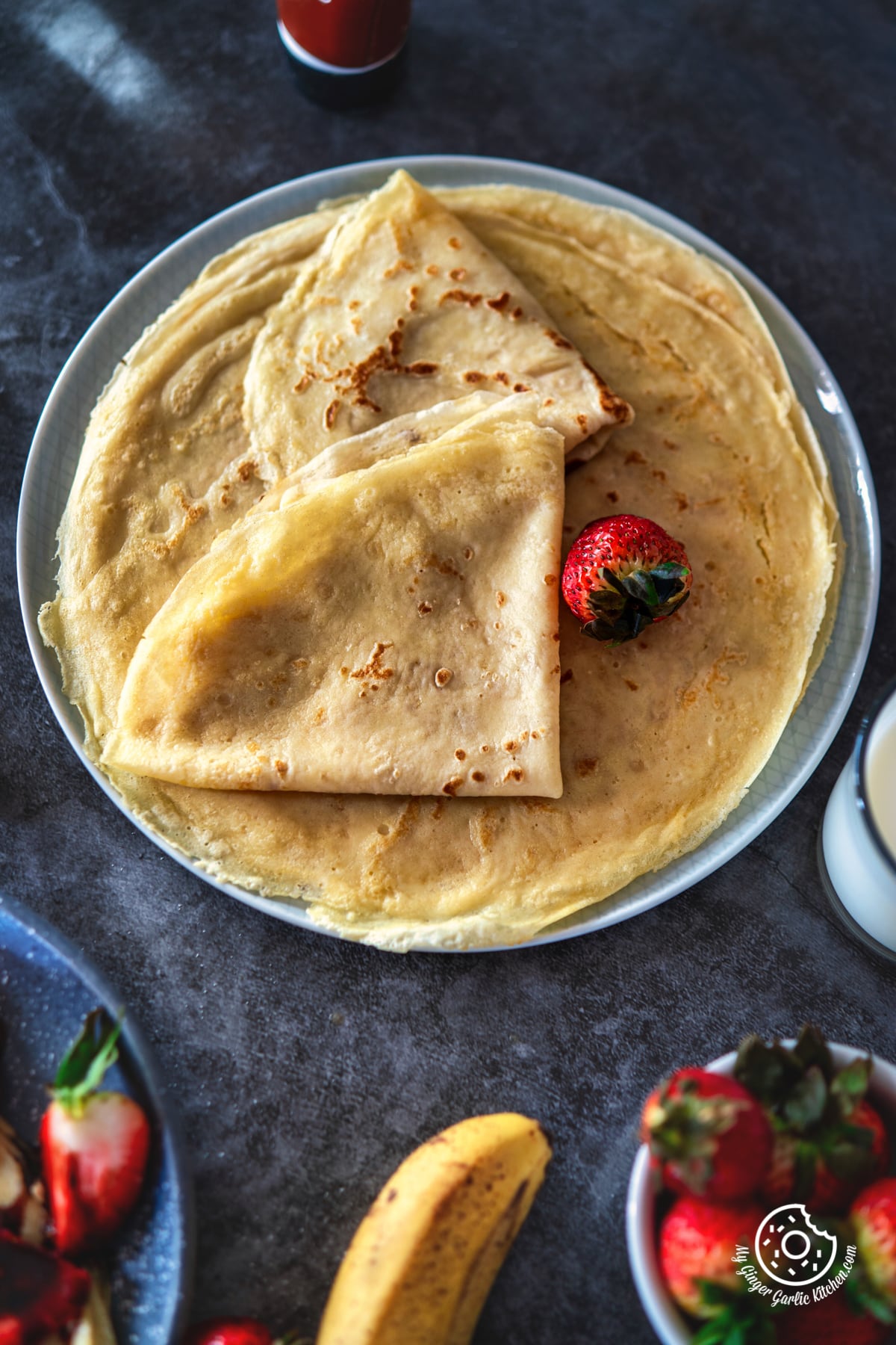 overhead shot of two folded sweet crepes along with a strawberry placed on a crepe filled plate