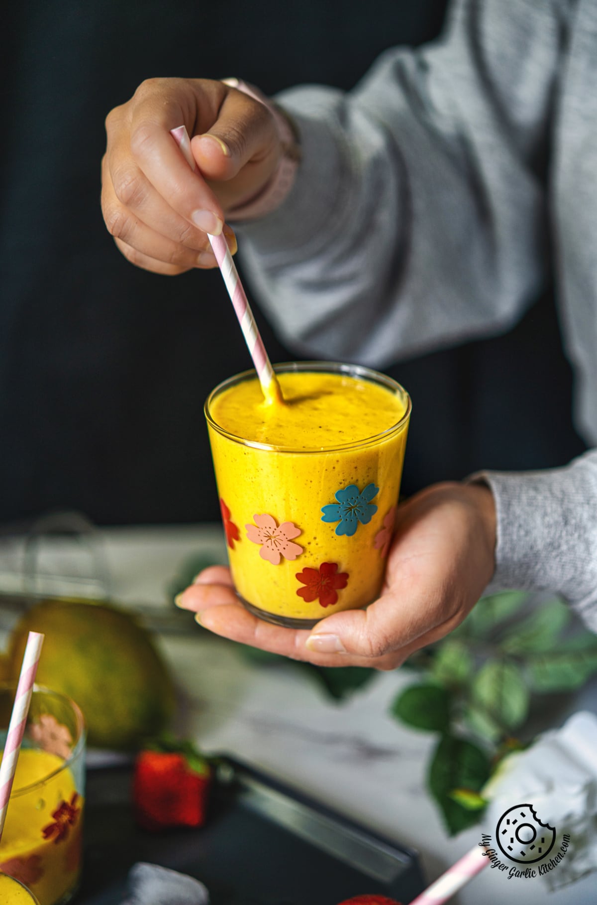 a female holding a mango smoothie glass with a straw