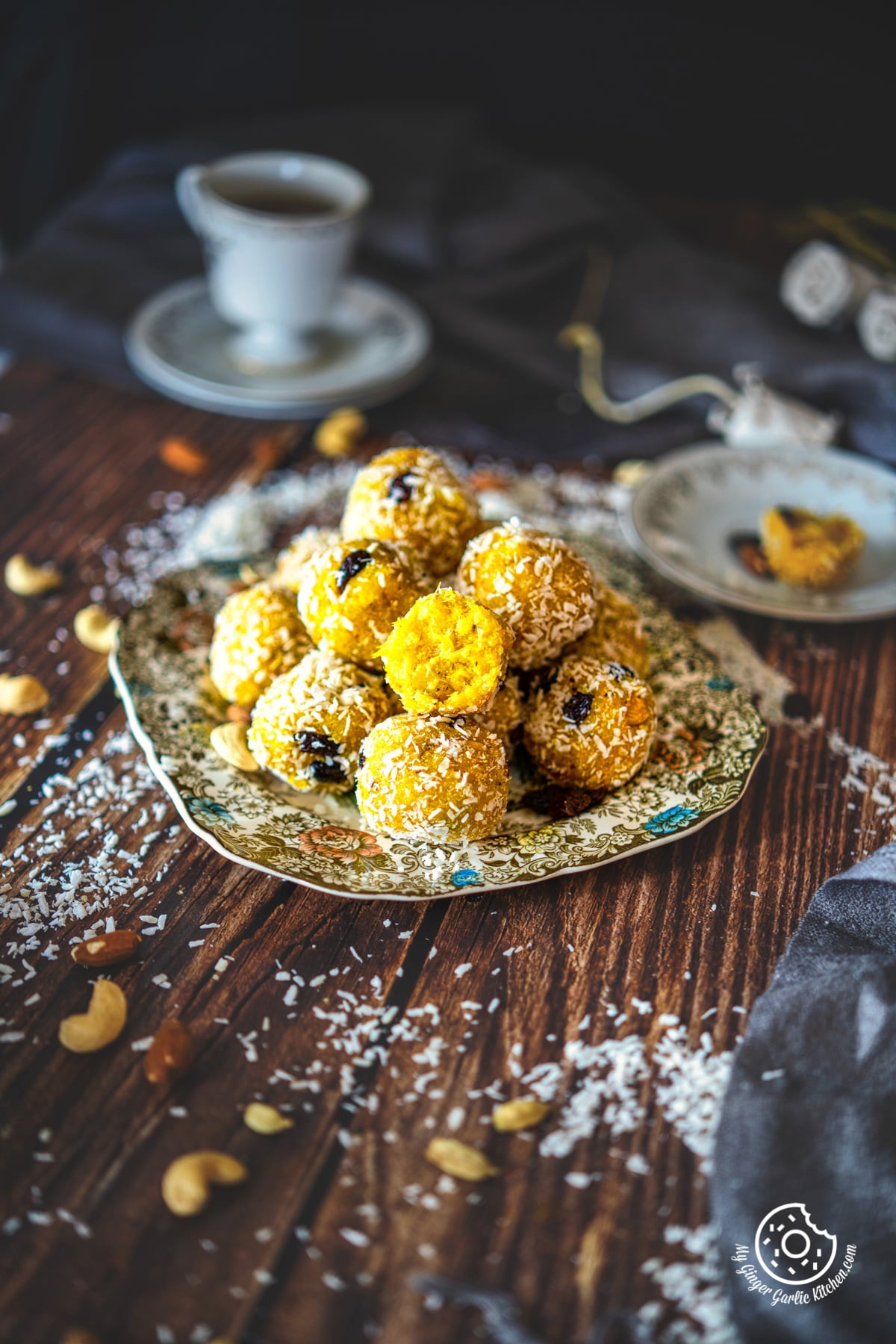 a stack of ladoos piled on floral plate with a tea cup in the background