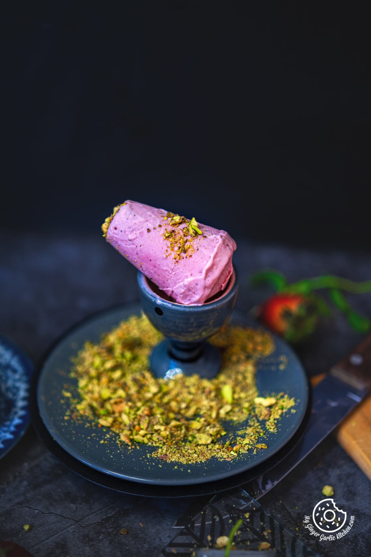 a strawberry kulfi served in a ceramic glass, topped with powdered pistachio nuts