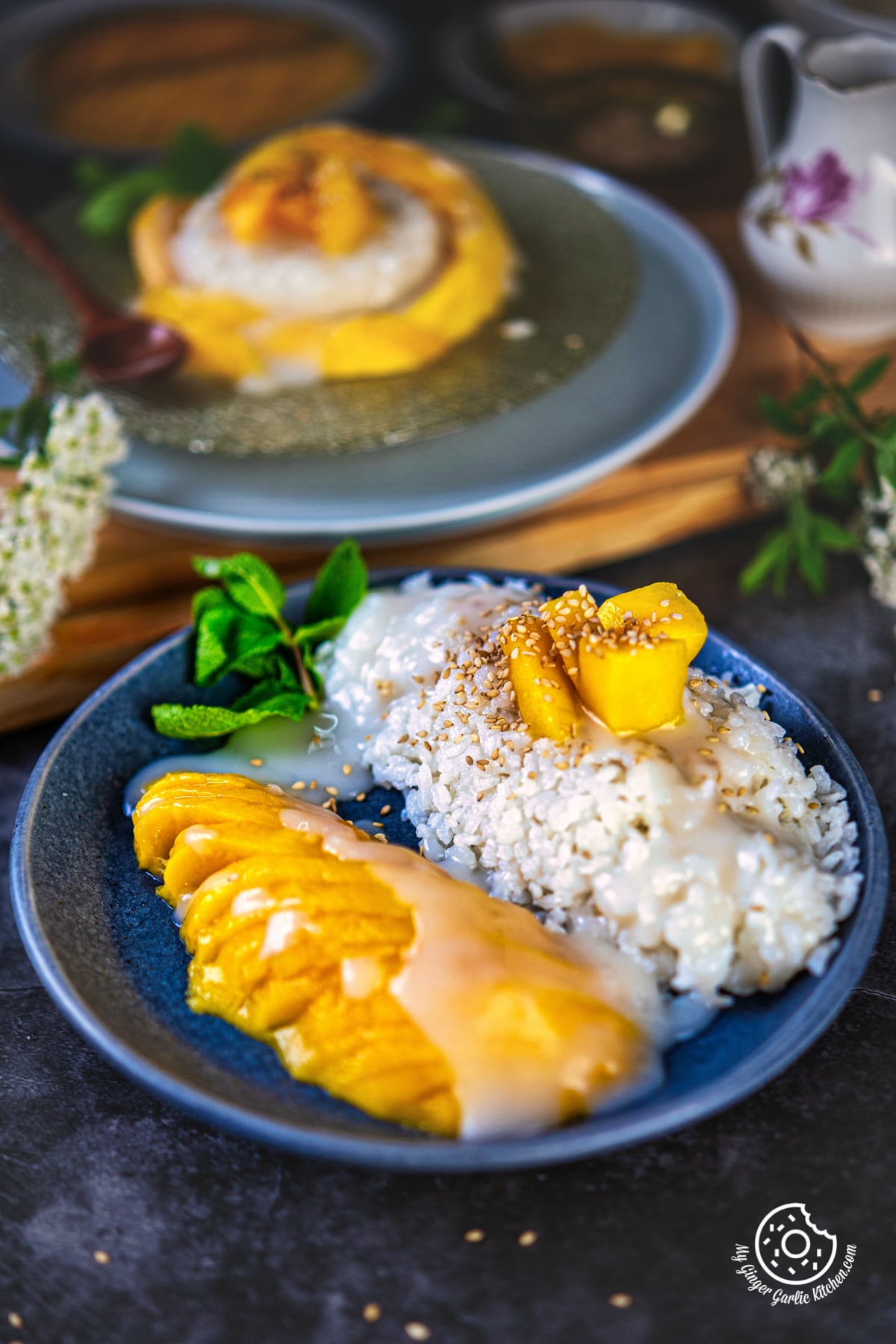 closeup shot of thai sticky mango rice topped with toasted sesame seeds and garnished with a mint sprig