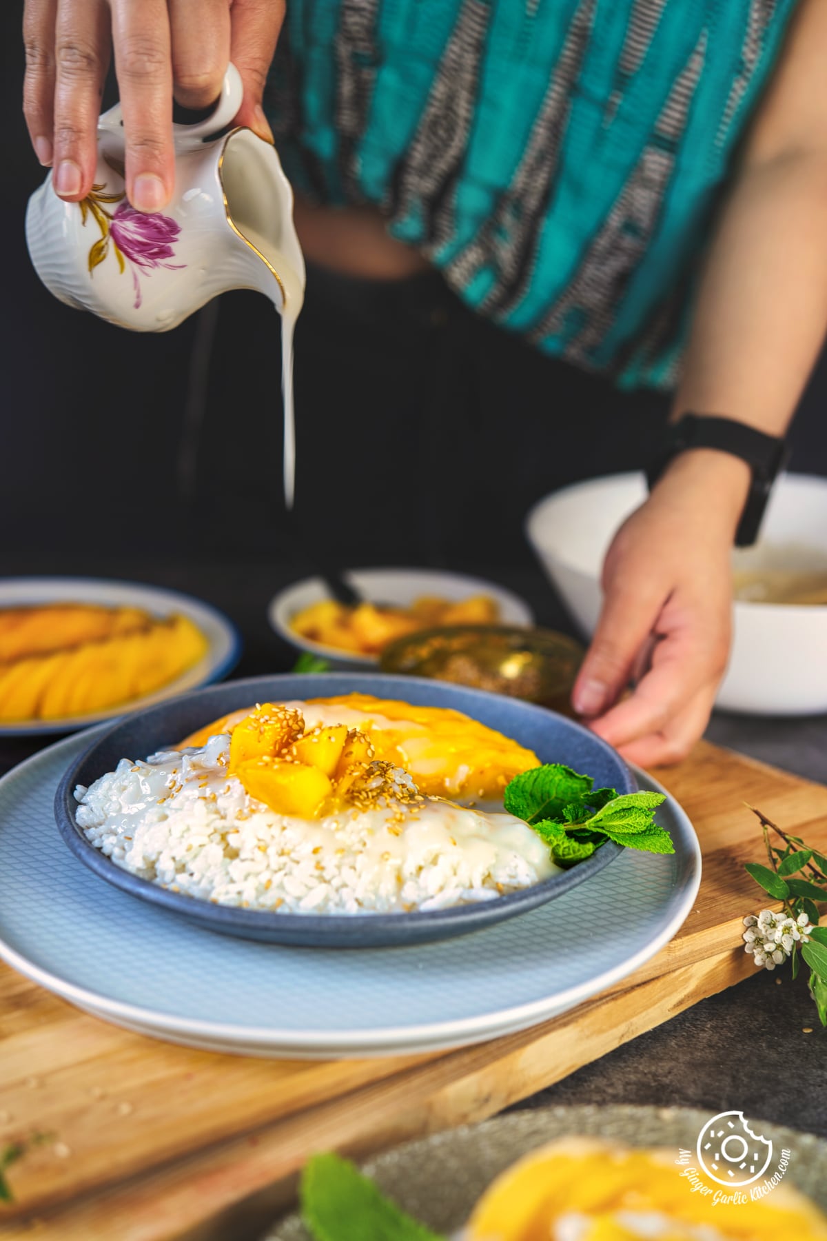 a female drizzling coconut sauce over thai sticky mango rice plate