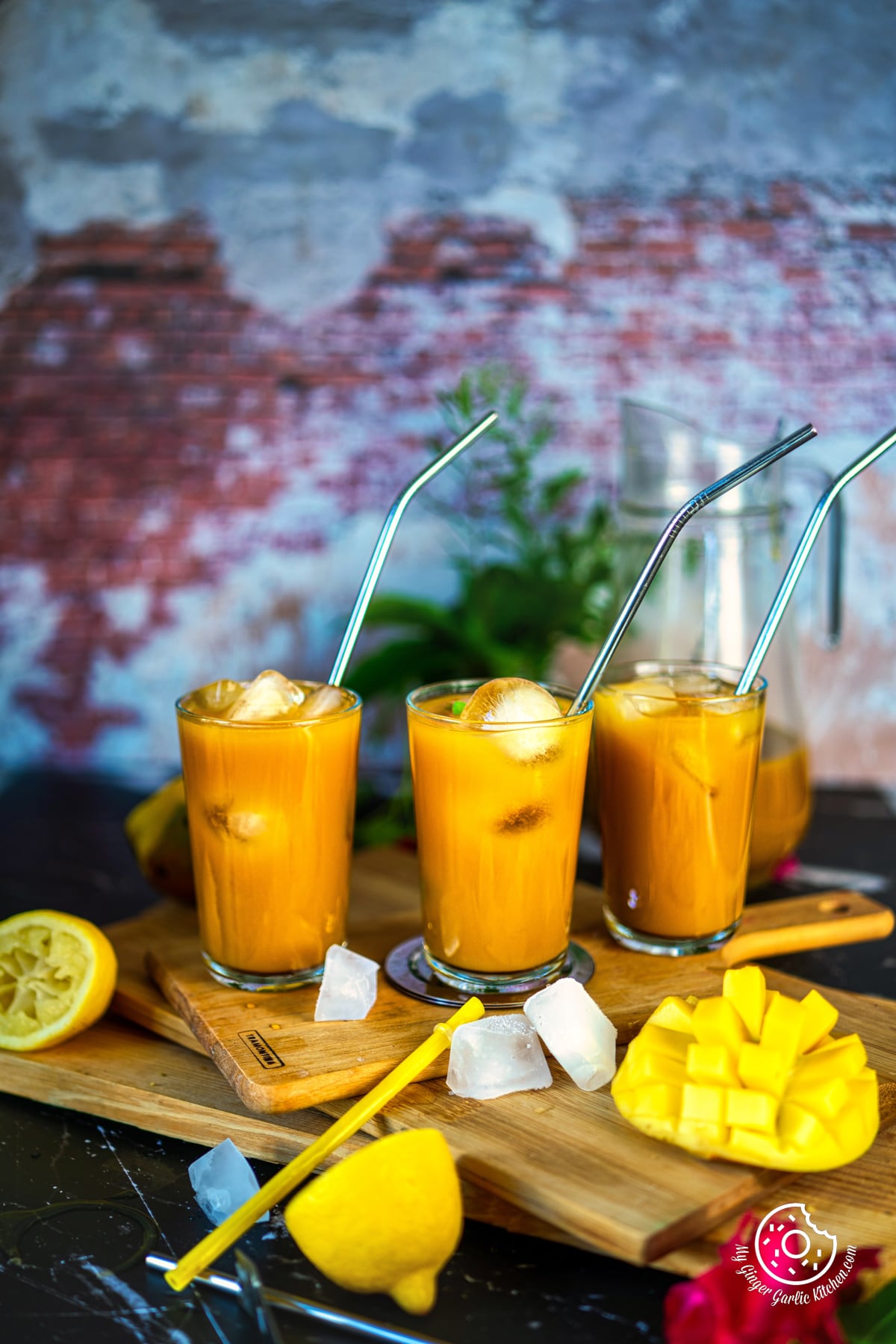 mango iced tea in three glasses with ice cubes on a wooden cutting board