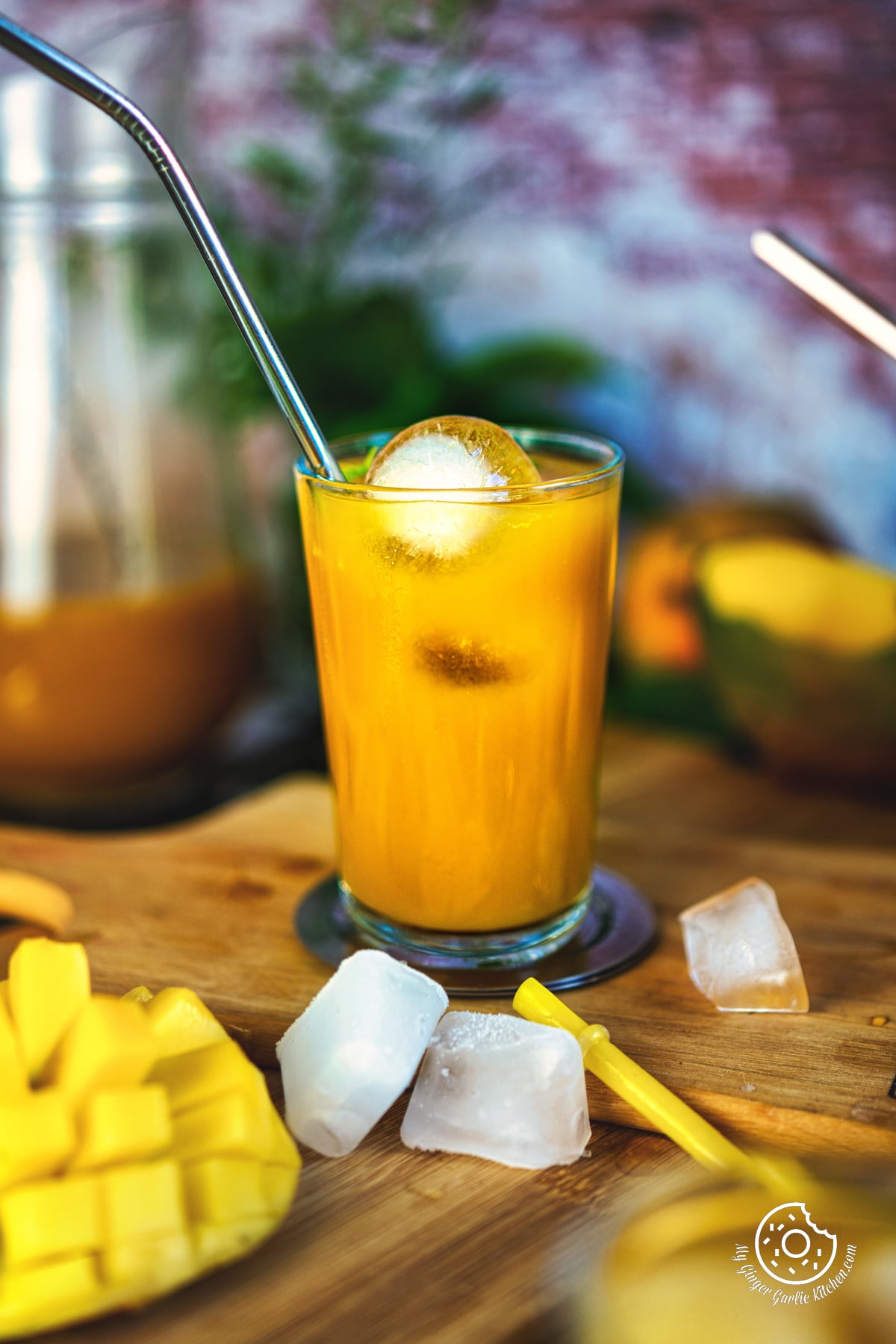 a glass of mango iced tea with ice cubes and a straw with mango slice and ice cubes on the side