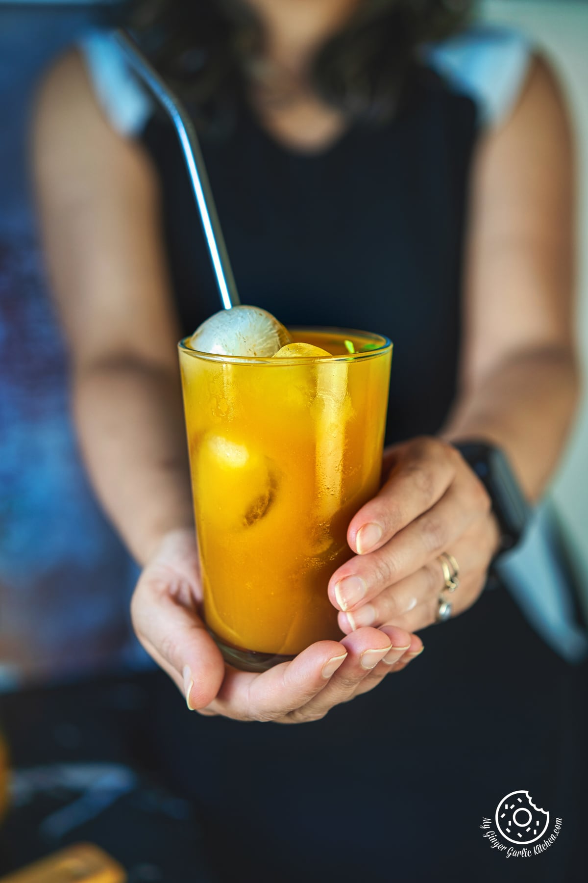 a female holding a mango iced tea glass with ice cubes and straw