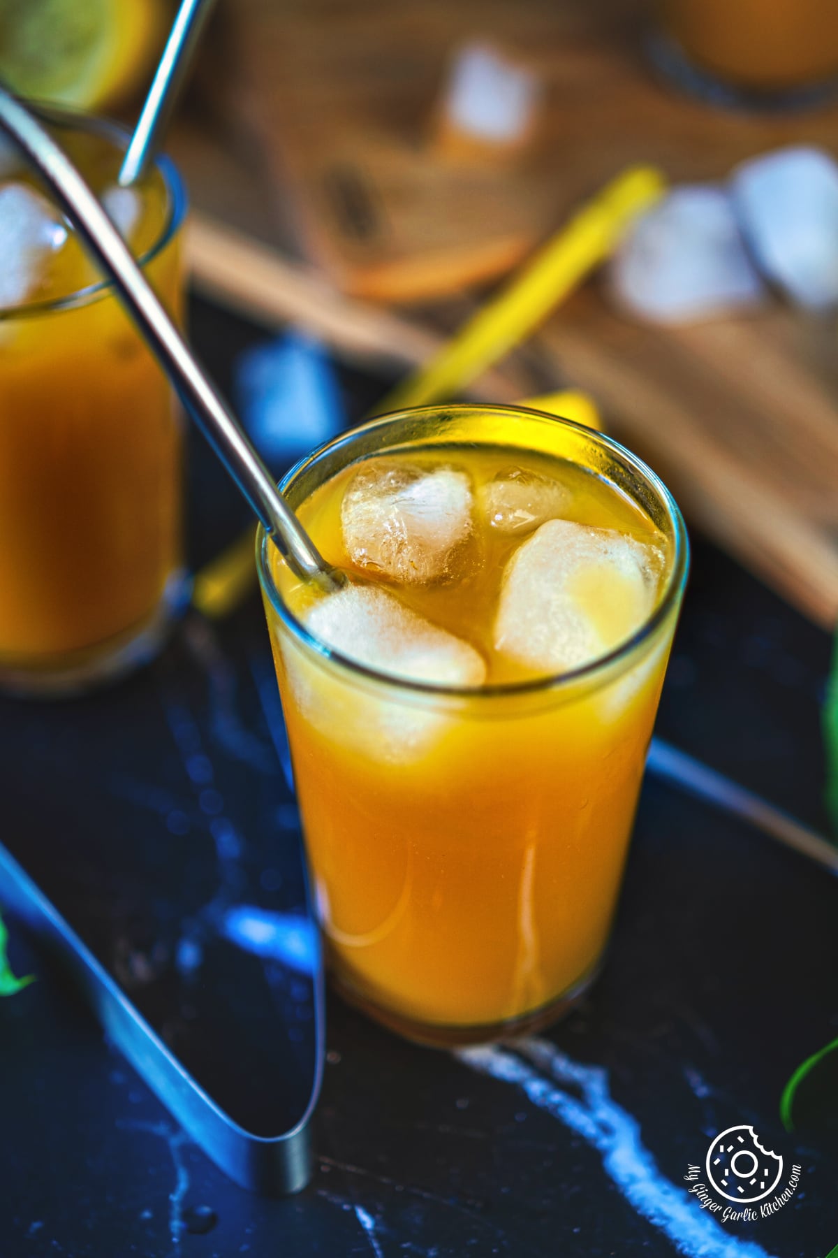 a closeup shot of mango iced tea in a tall glass with ice cubes and a straw
