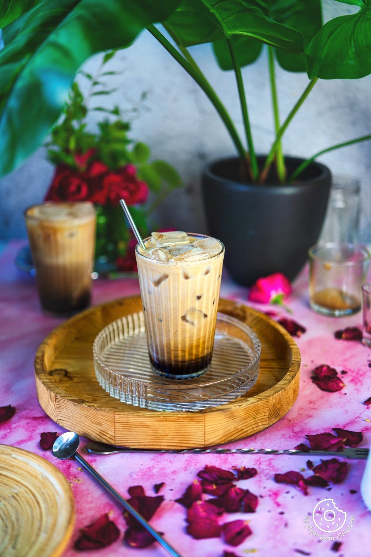 Picture of iced rose latte glass with some rose petals and flowers.