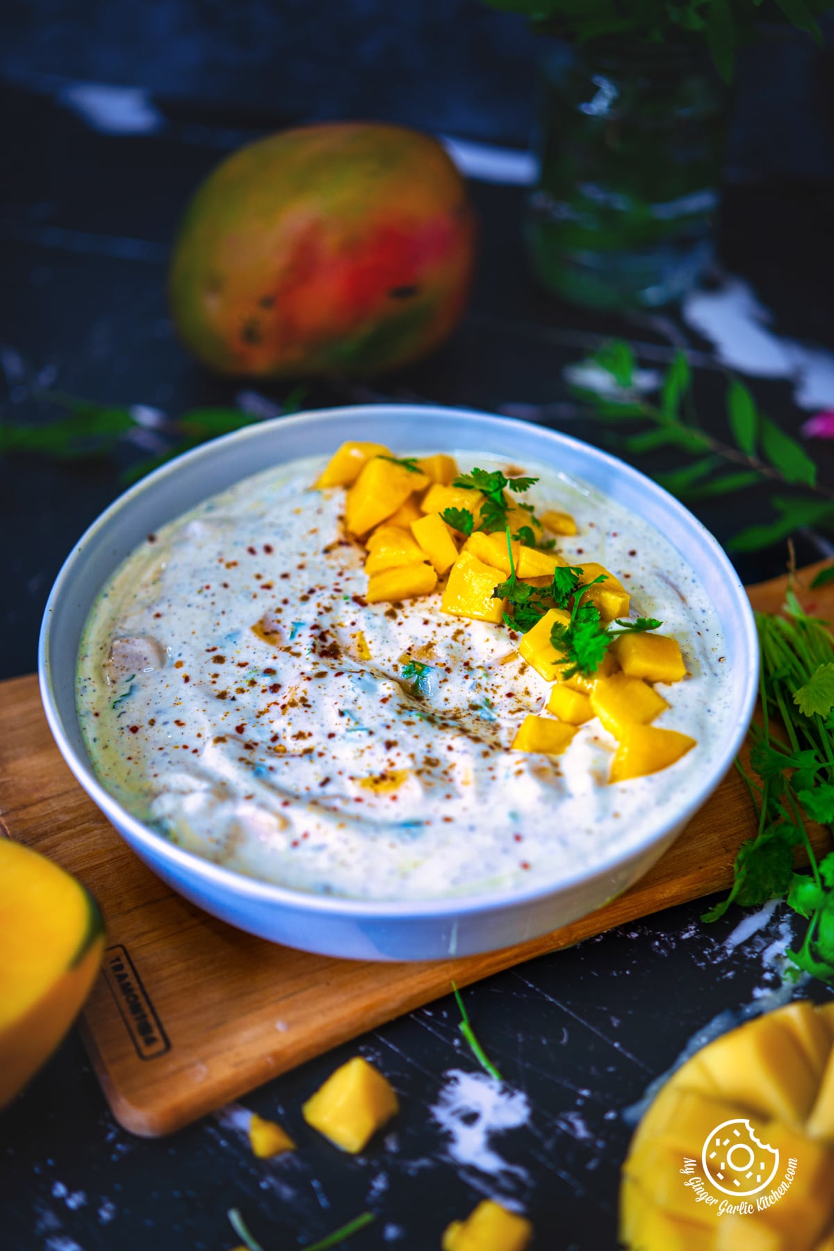 mango raita served in a grey ceramic bowl topped with mango chunks and garnished with fresh cilantro