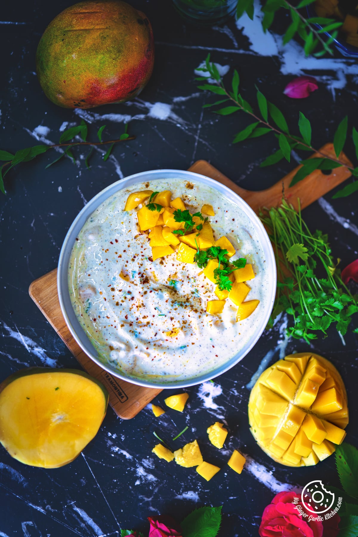 flatlay of mango raita served in a grey ceramic bowl with mangoes on the side