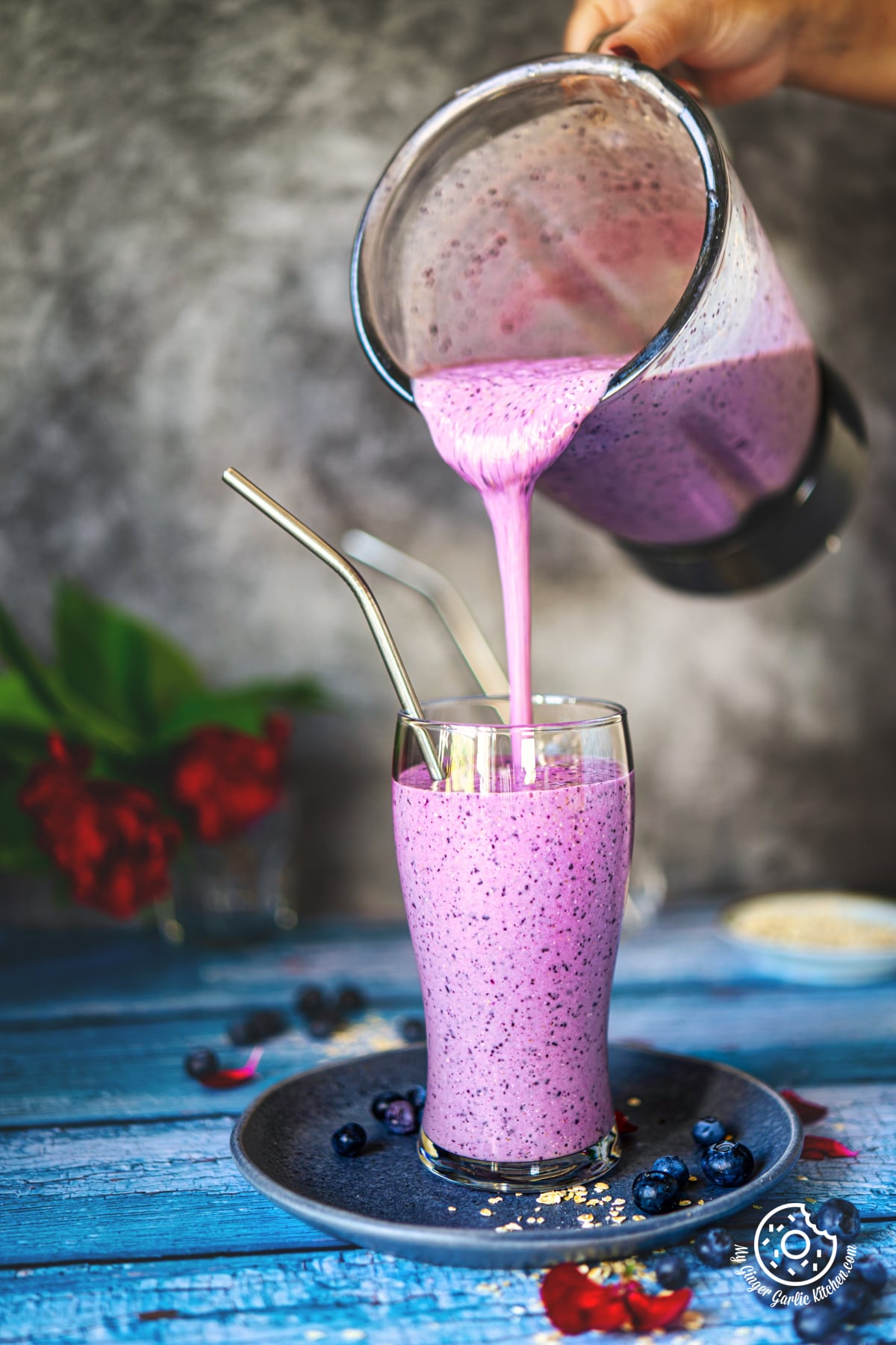a hand pouring healthy blueberry pie smoothie in a glass from a blender jar
