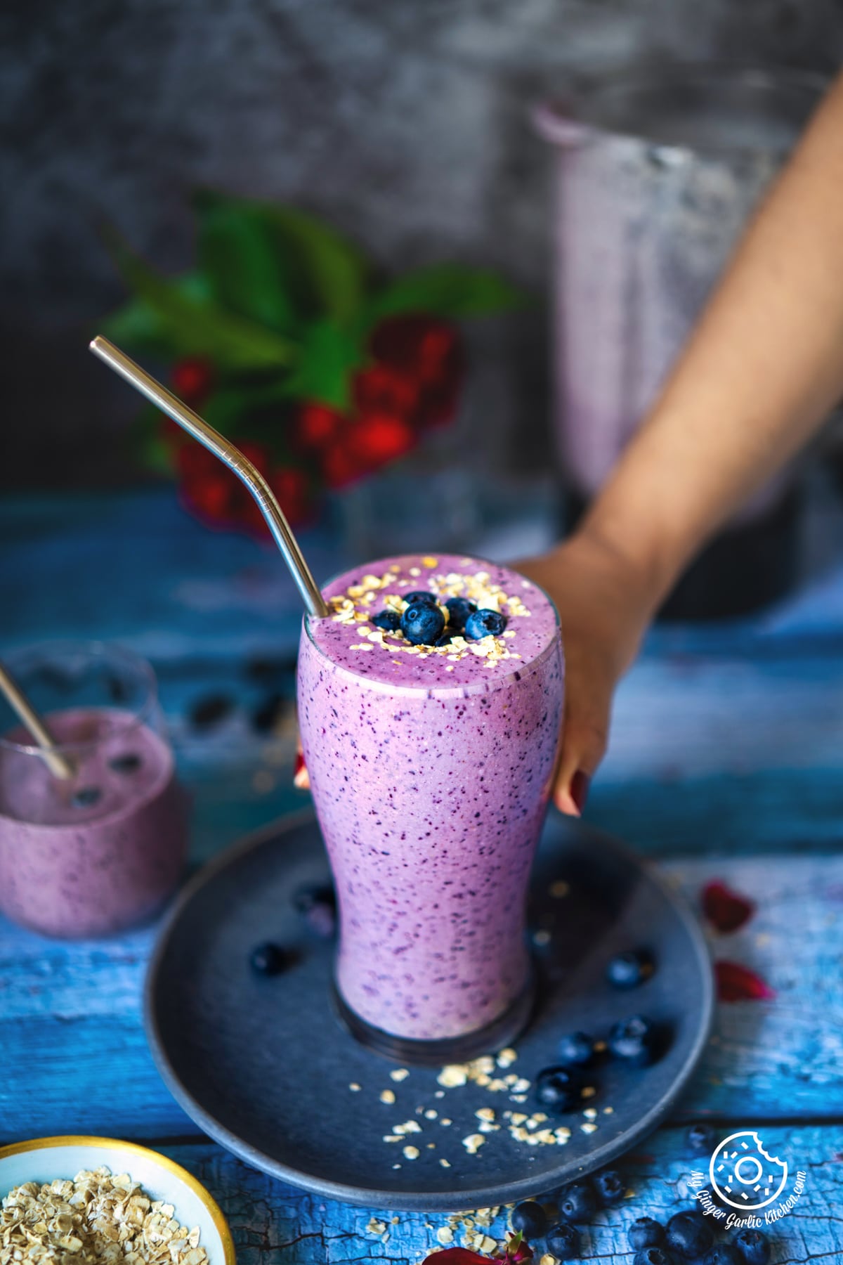 a hand holding healthy blueberry pie smoothie glass topped with blueberries and oats