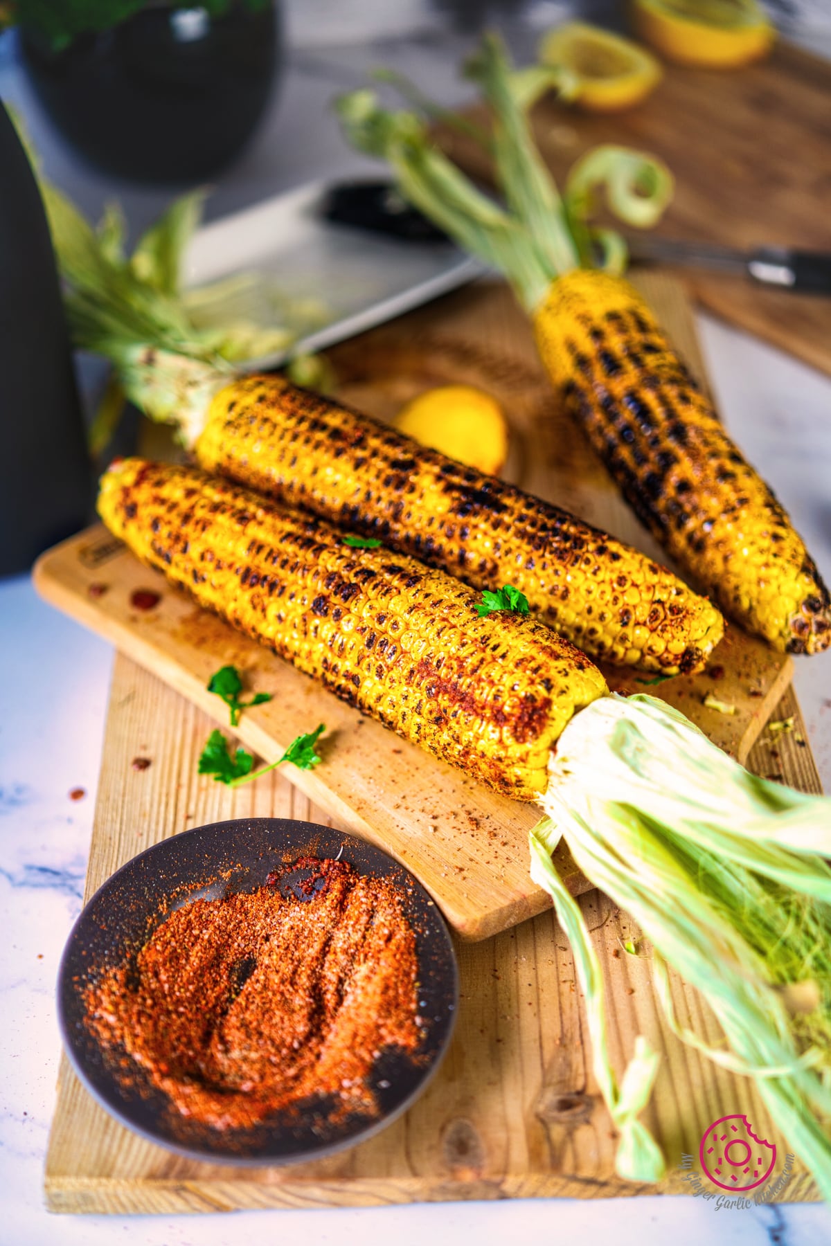 3 indian roasted corn on the cobs or masala bhutta on a wooden board with a bowl of spice