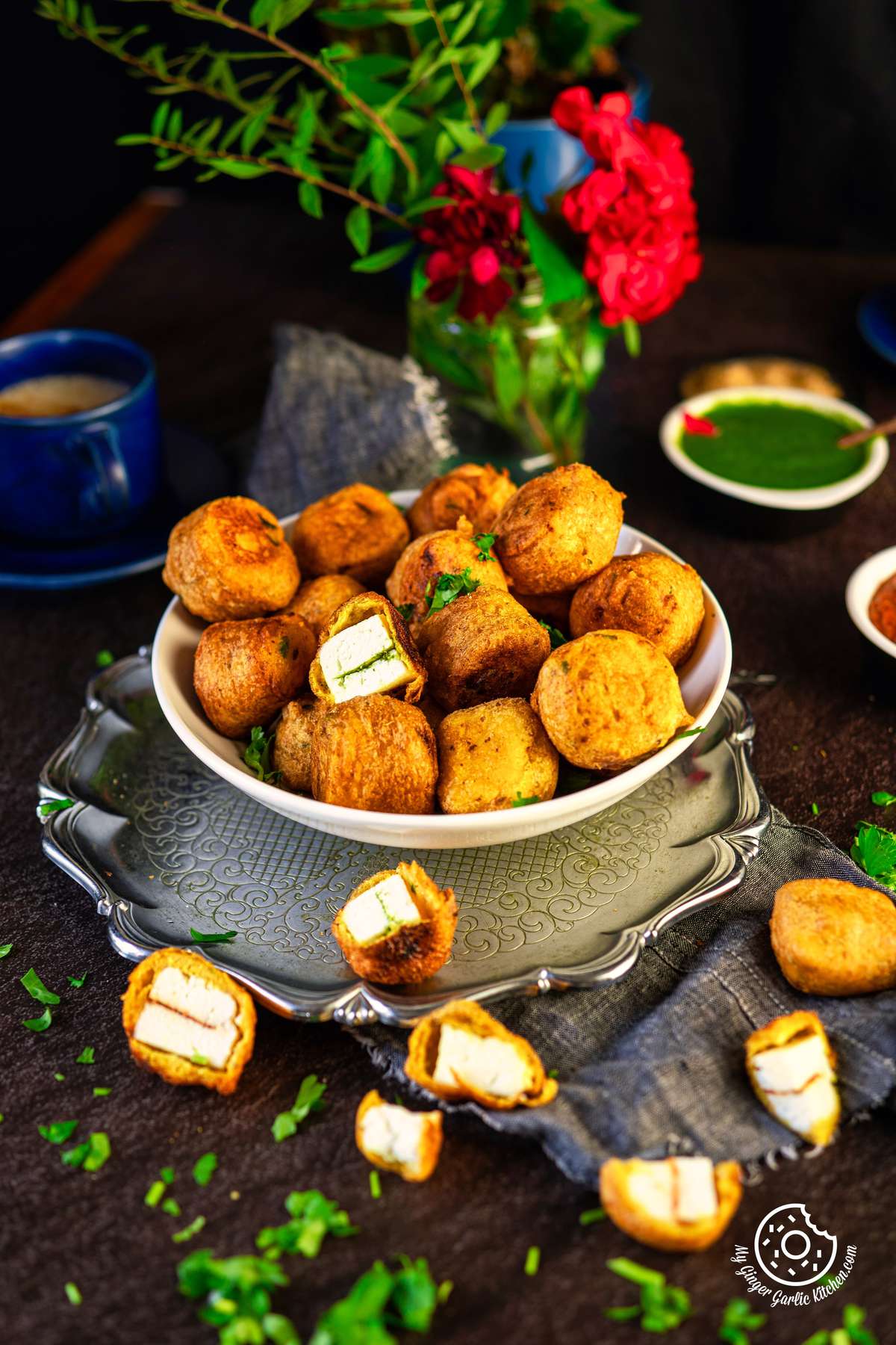 paneer pakoras served on a white plate and some pakoras scattered on the side with mint chutney in a small bowl