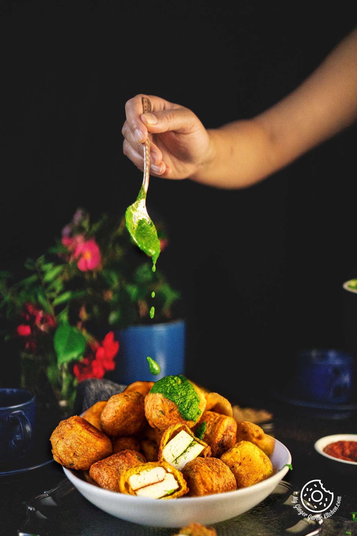 a hand drizzling green chutney over paneer pakora served on a bowl