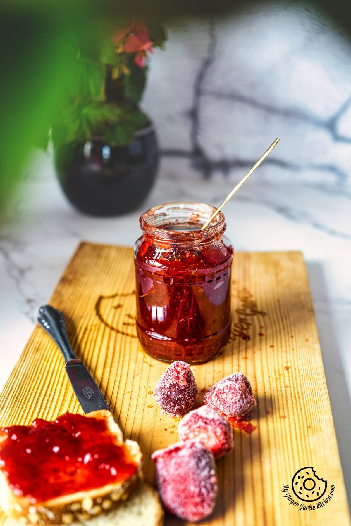 strawberry jam in a glass jar with knife and some strawberries on the side