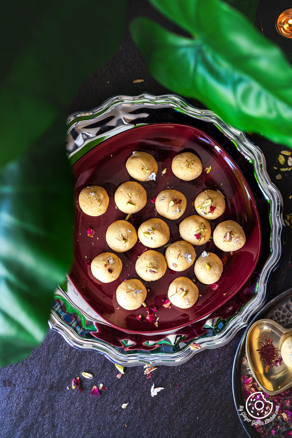 overhead shot of 16 malai ladoo in a maroon plate with dried saffron strands on the side