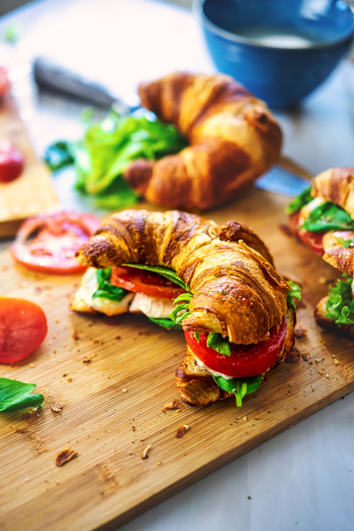 a female holding 1 caprese croissant sandwich on a wooden board with one more sandwich on the side