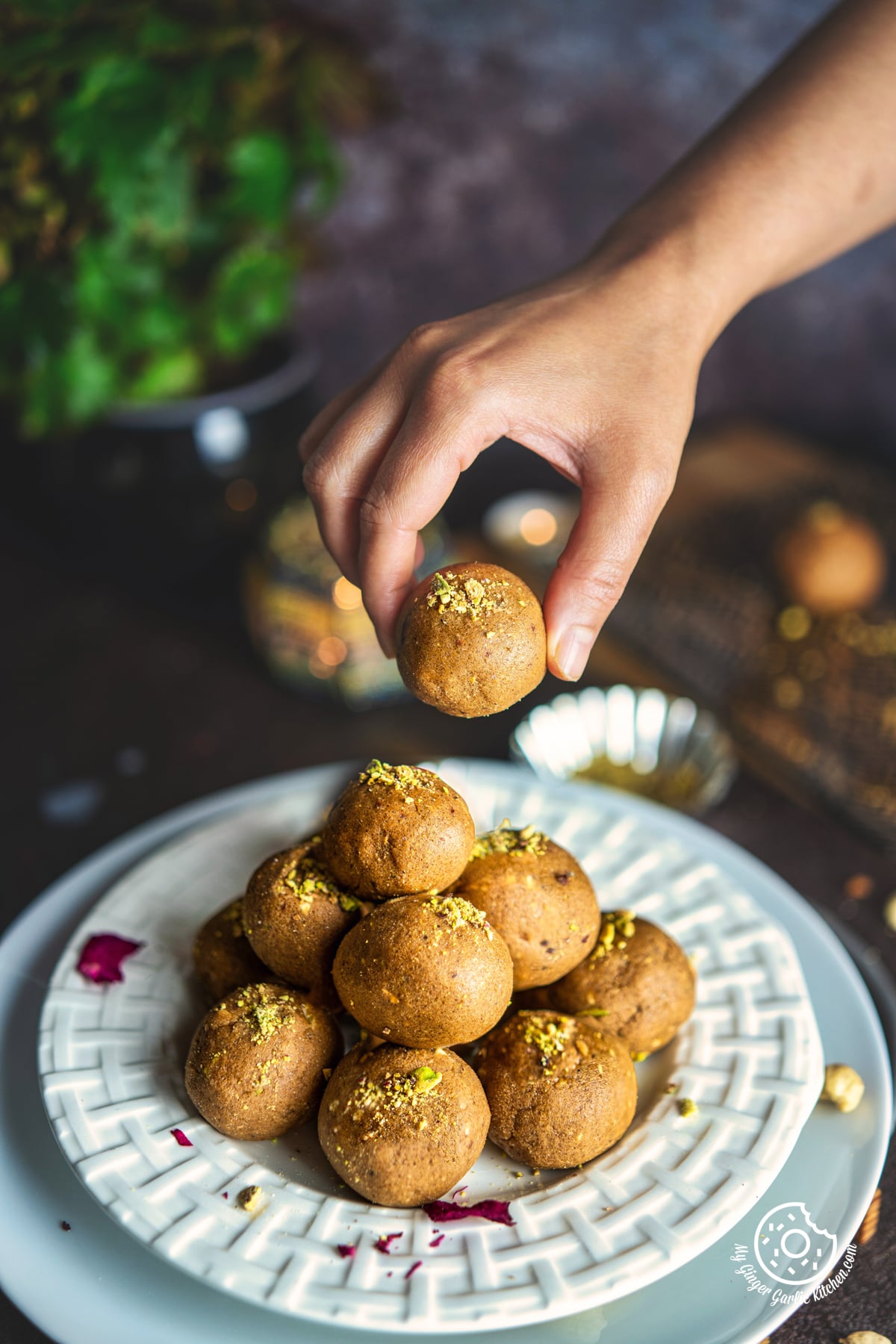 a hand picking one atta ladoo from the white plate stacked with atta ladoos