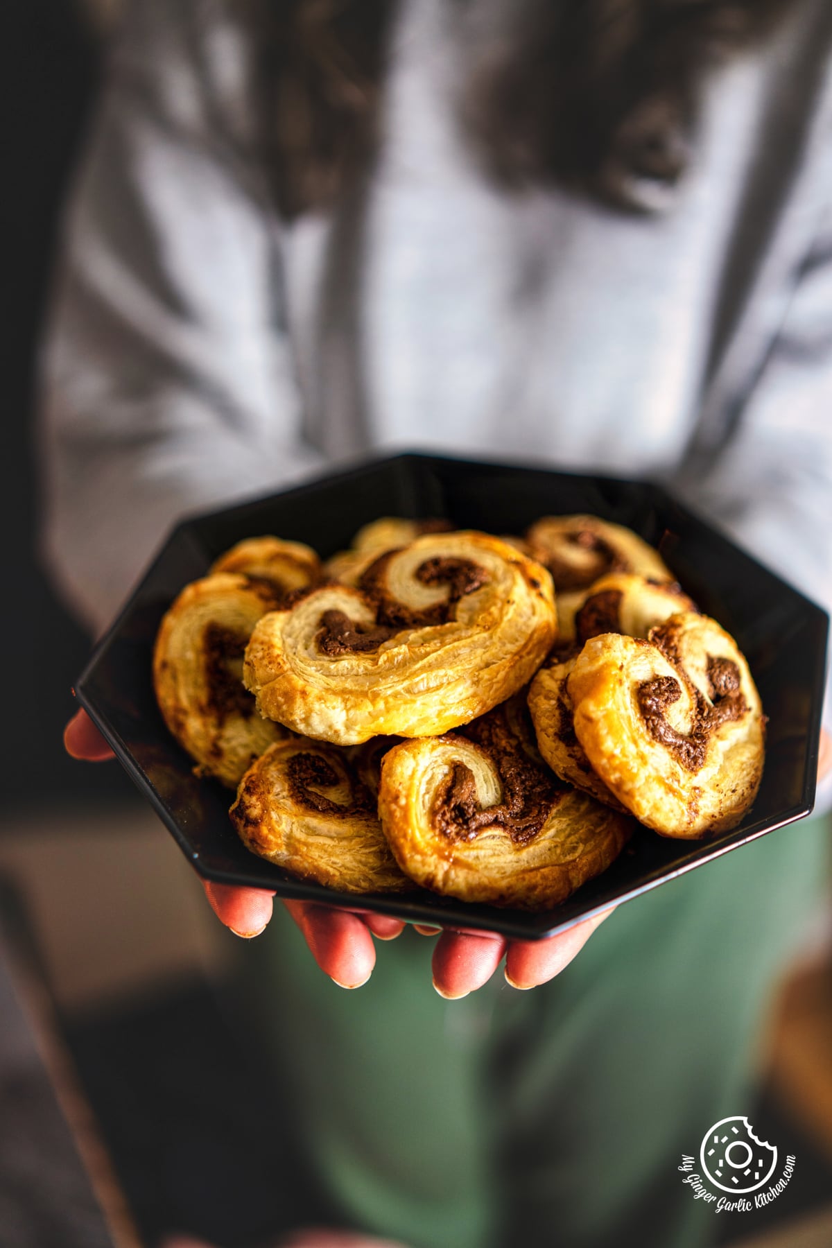 a closeup of a female holding black plate with chocolate palmiers