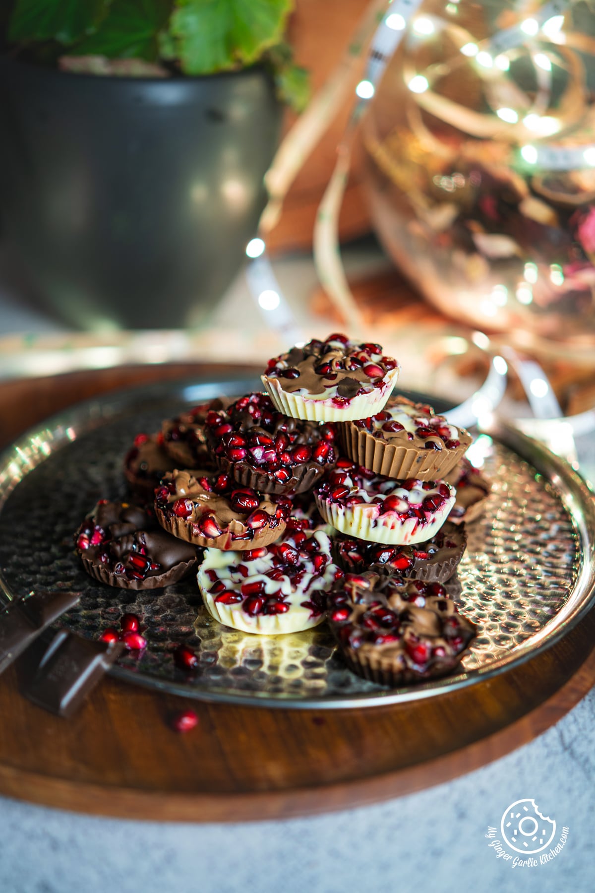 a stack of assorted chocolate pomegranate bites on a metal plate with some lights in the background