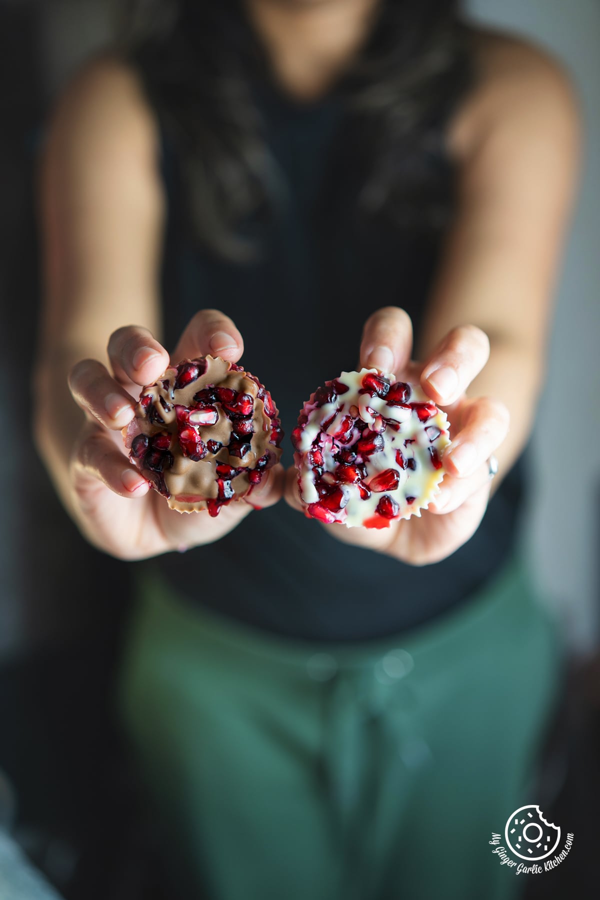 a close up of female holding two chocolate pomegranate bites in both the hands