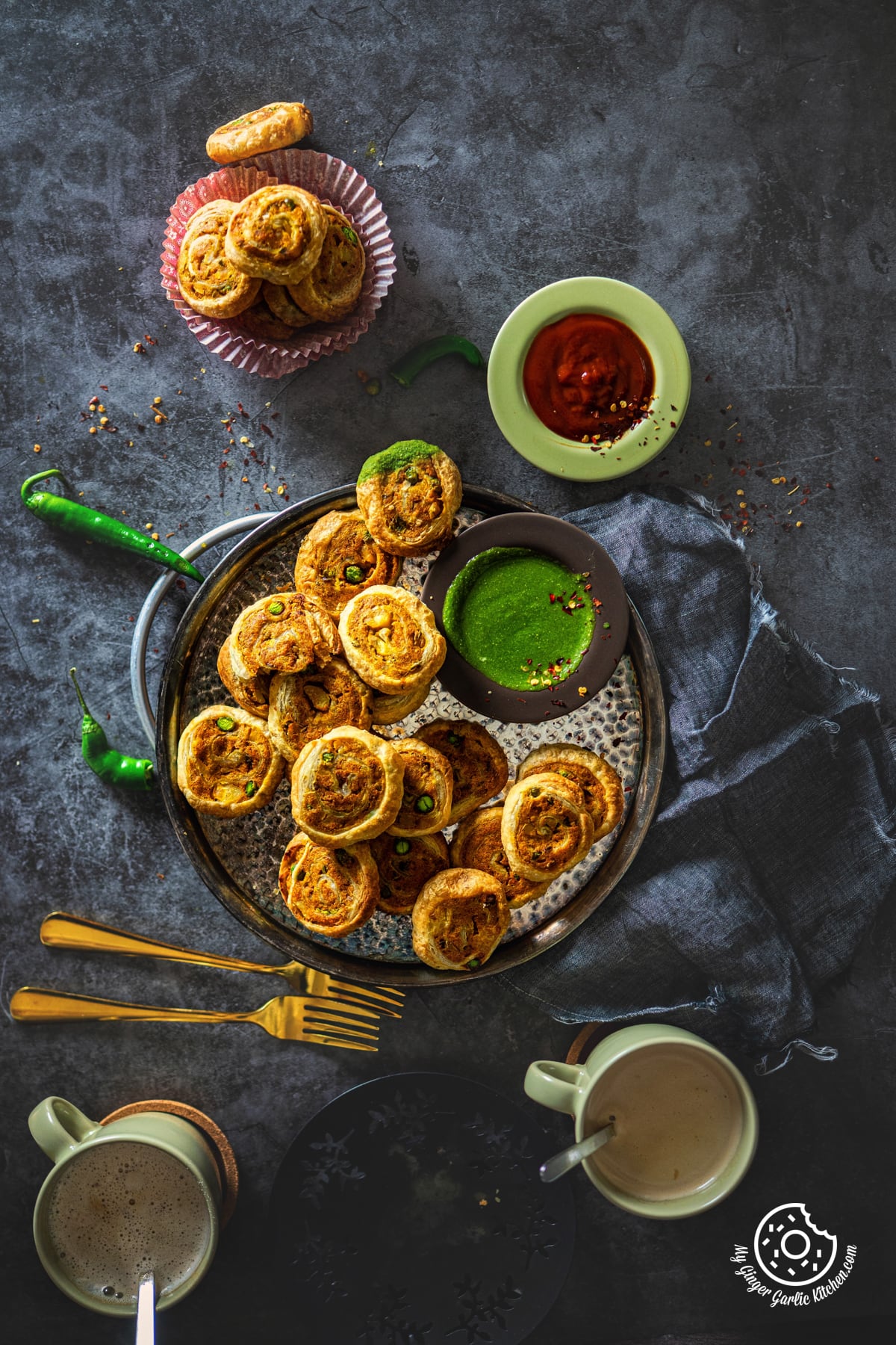 overhead photo of samosa pinwheels in a metal plate with green chutney and tomato ketchup on the side